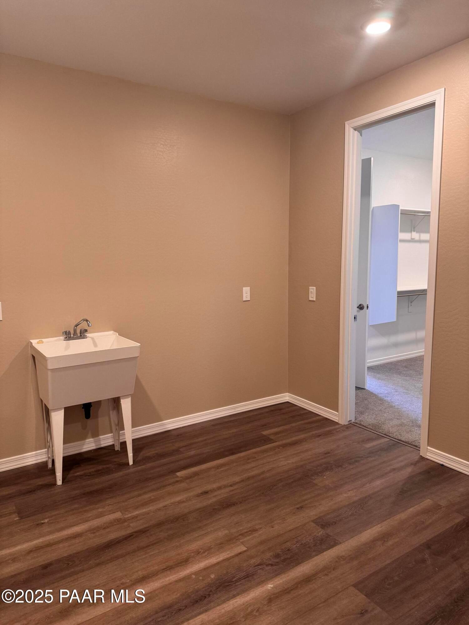 Spacious laundry room featuring white utility sink, beige walls, and laminate wood floors in Davidson Homes Sunrise II A, Prescott, AZ