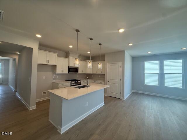 Modern open-concept kitchen with white cabinets, quartz island, stainless appliances, and pendant lights in The Daphne C 4-bedroom home, Zebulon, NC