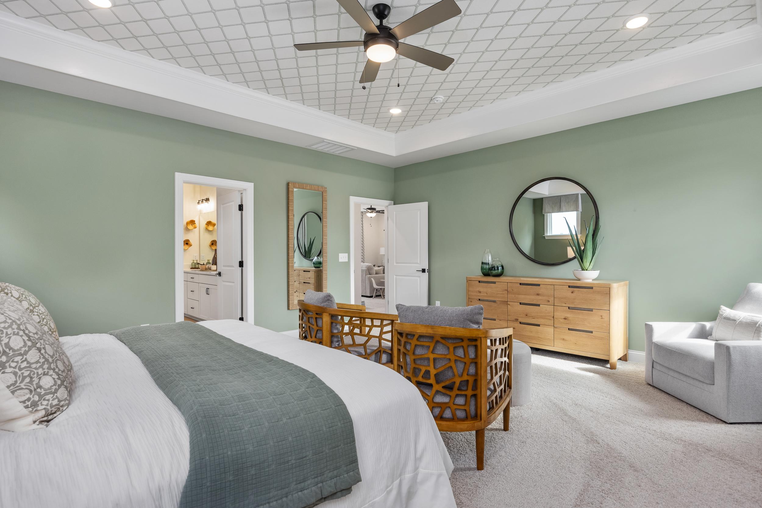 Spacious primary bedroom at Laneridge Estates in Raleigh NC with sage green walls, king bed, tufted armchair, and en-suite bath