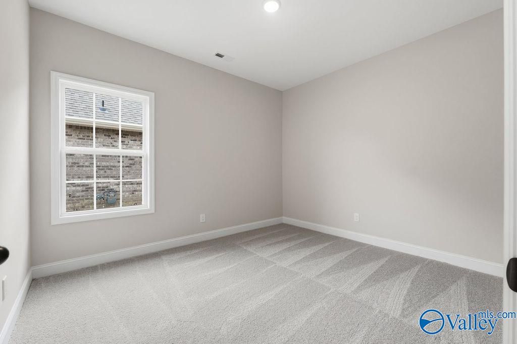 Empty secondary bedroom with light gray walls, large grid window, and plush carpet in Davidson Homes The Rockford B, Hartselle, AL
