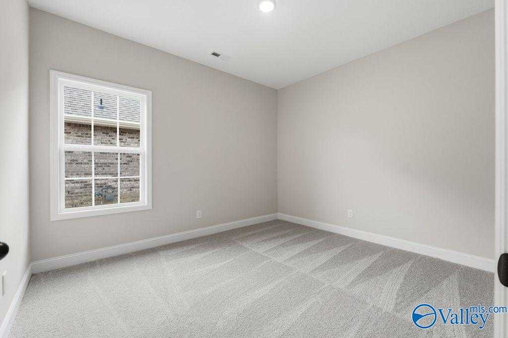 Empty secondary bedroom with light gray walls, large grid window, and plush carpet in Davidson Homes The Rockford B, Hartselle, AL