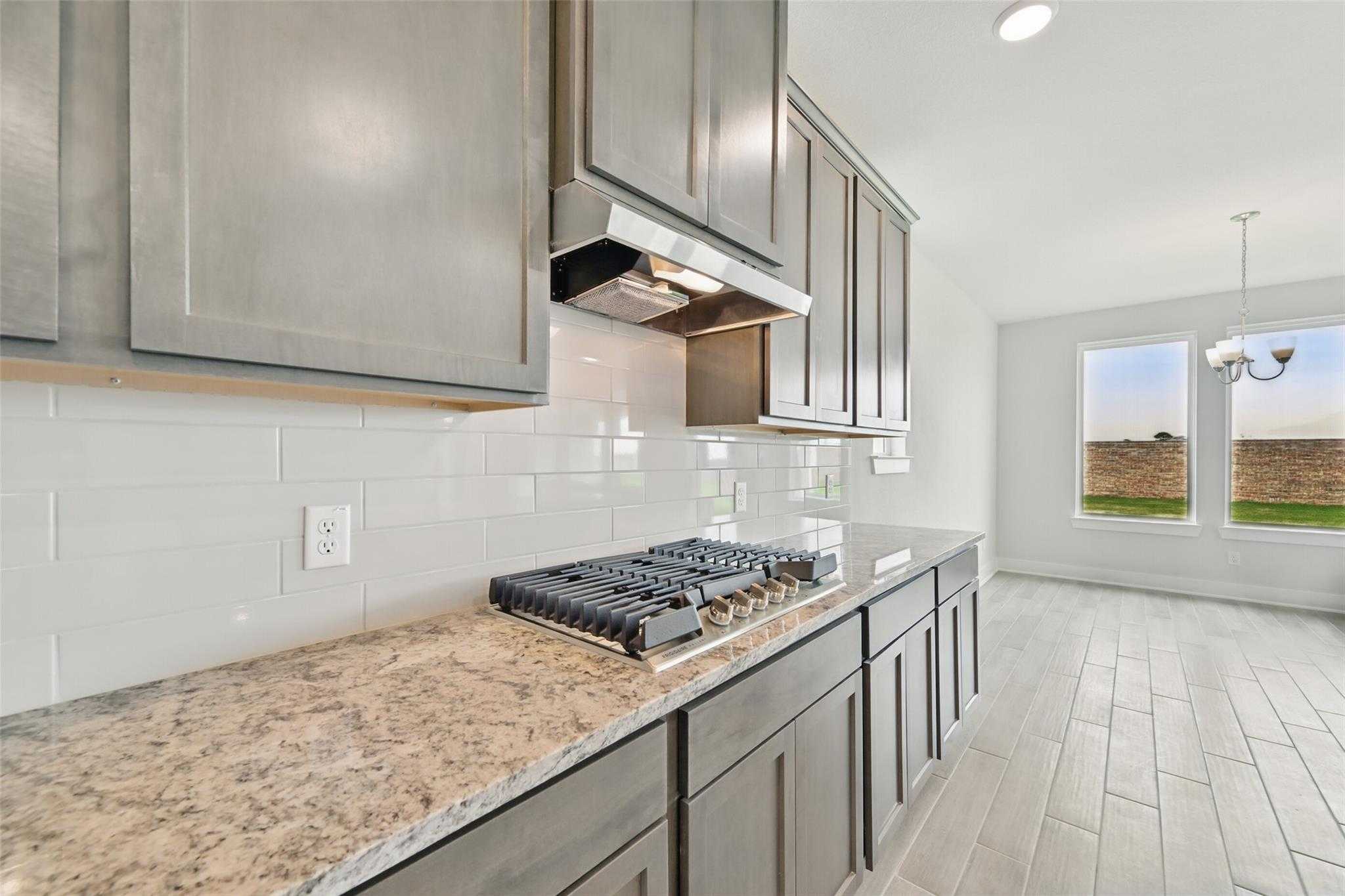 Modern kitchen featuring gray shaker cabinets, granite counters, subway tile backsplash, gas range in Davidson Homes The Philip A, Lago Mar