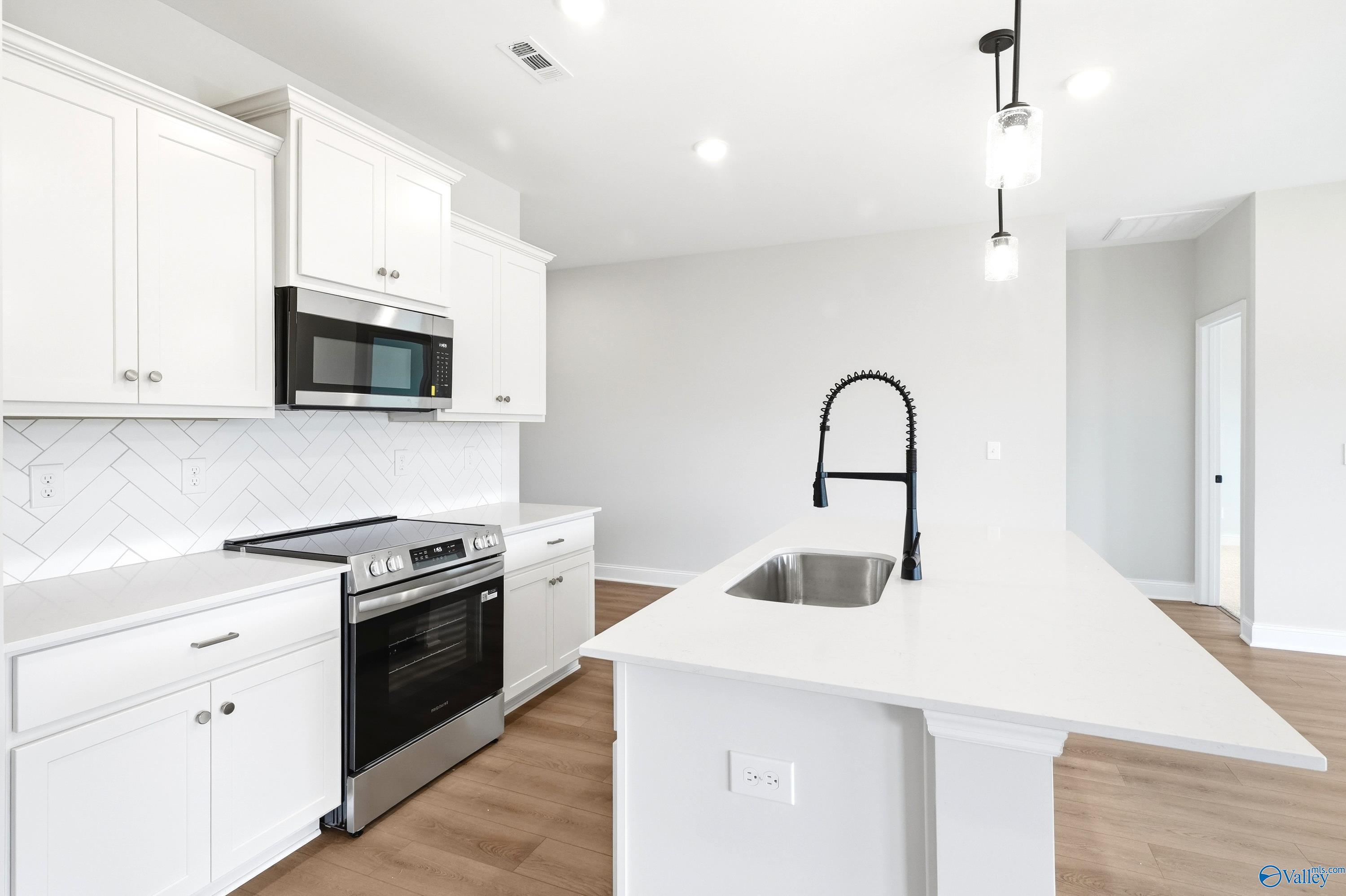 Modern kitchen with white cabinets, quartz island, and stainless steel appliances in The Daphne floor plan, Meridianville.