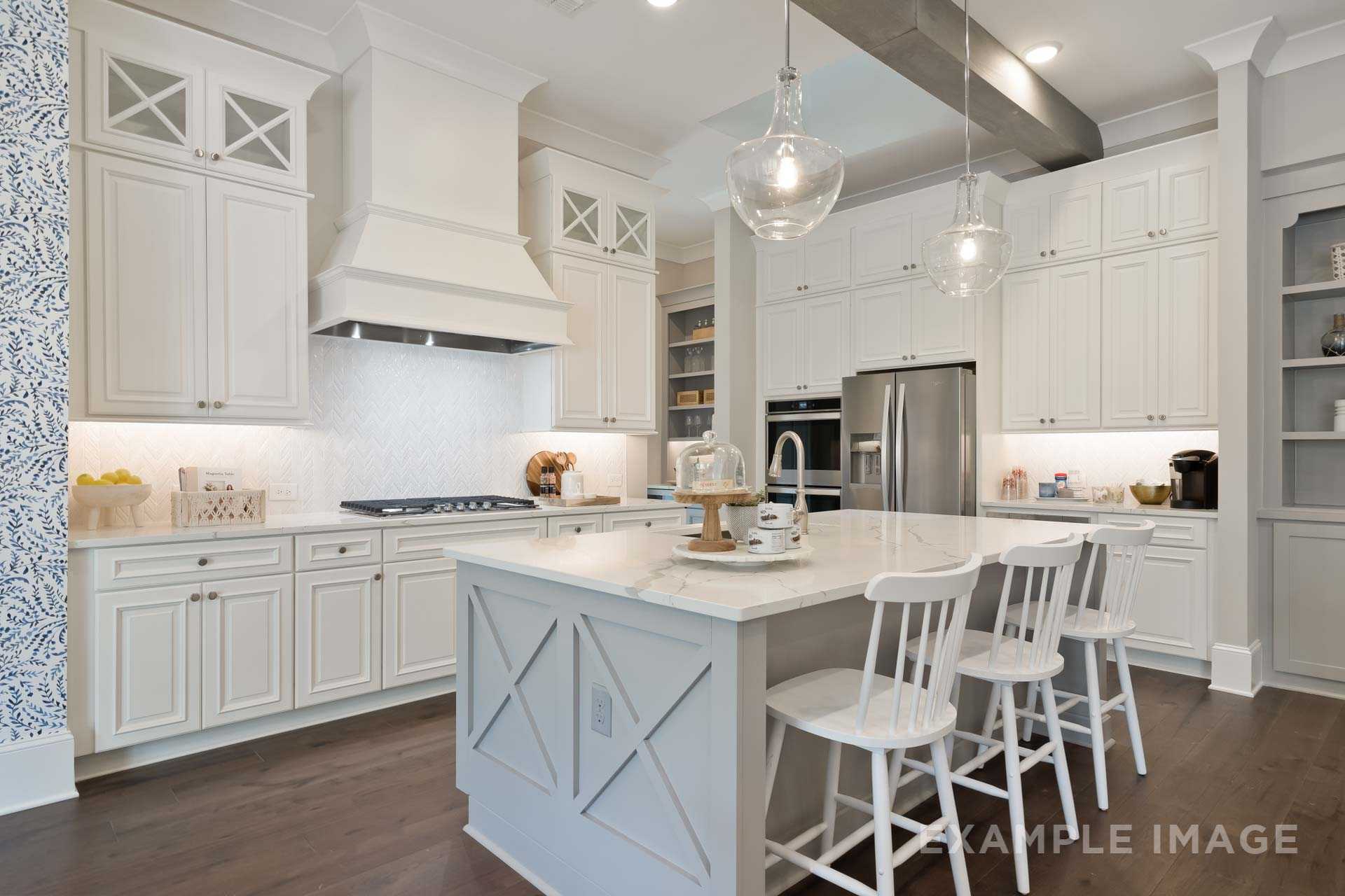Spacious white kitchen in The Seaside home with shaker cabinets, large island, stainless appliances, and pendant lights