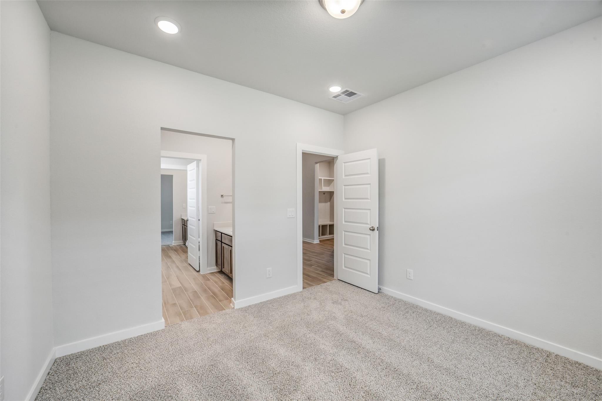Spacious bedroom with carpet flooring, open doors to bathroom vanity and closet in Davidson Homes The Acadia C, Magnolia TX