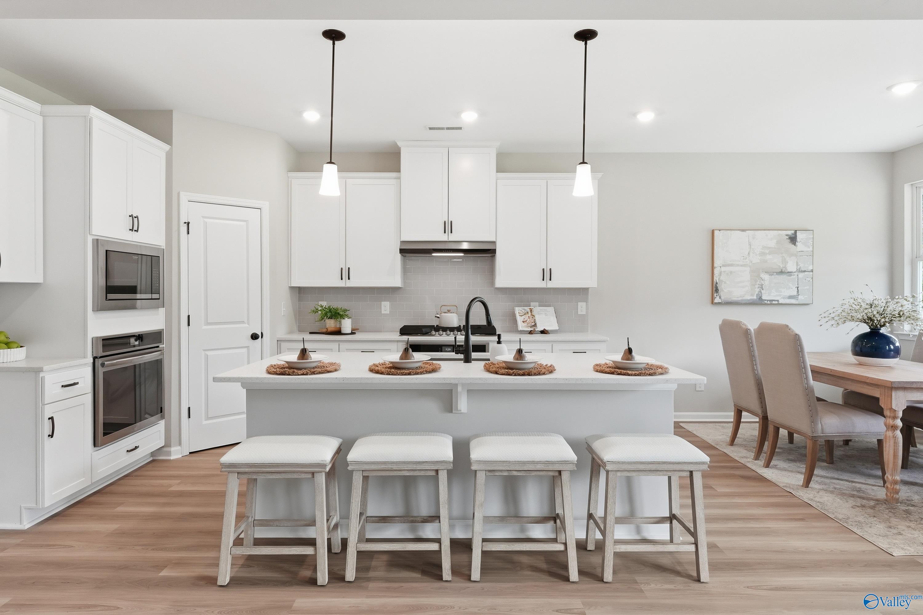 Modern white shaker kitchen with quartz island, bar stools, stainless appliances, adjacent dining area in Davidson Homes The Dorado, Huntsville AL