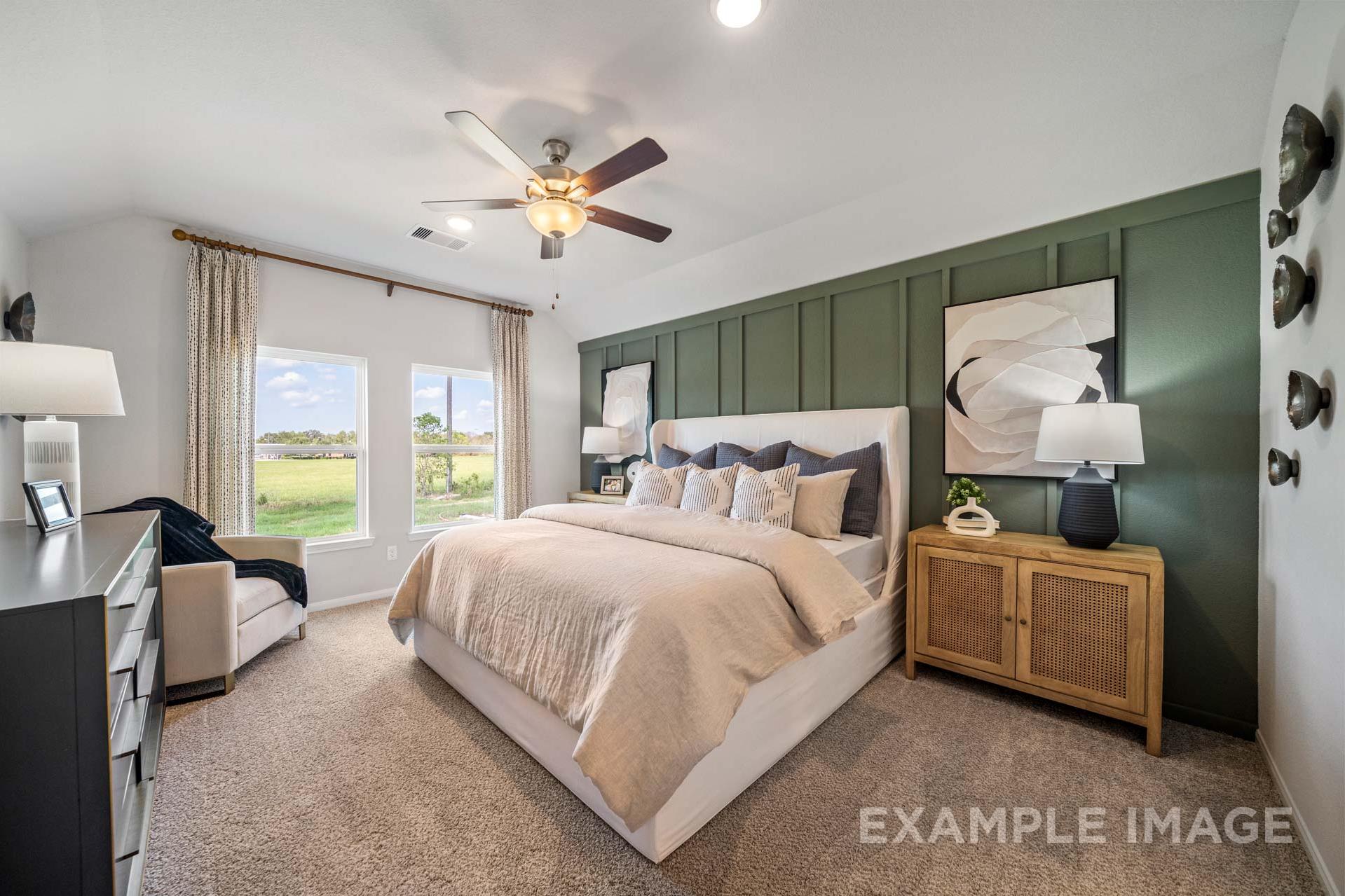 Spacious master bedroom in The Acadia A with king bed, green accent wall, large windows overlooking fields, ceiling fan