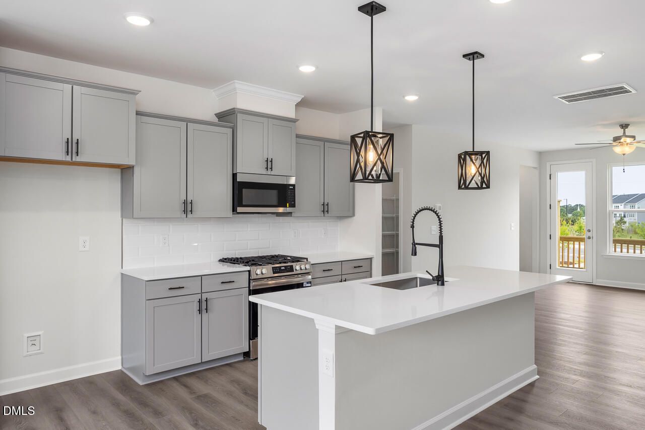 Modern kitchen with gray cabinets, quartz island, and pendant lights in The Mitchell floor plan, Forestville Yard Townhomes.