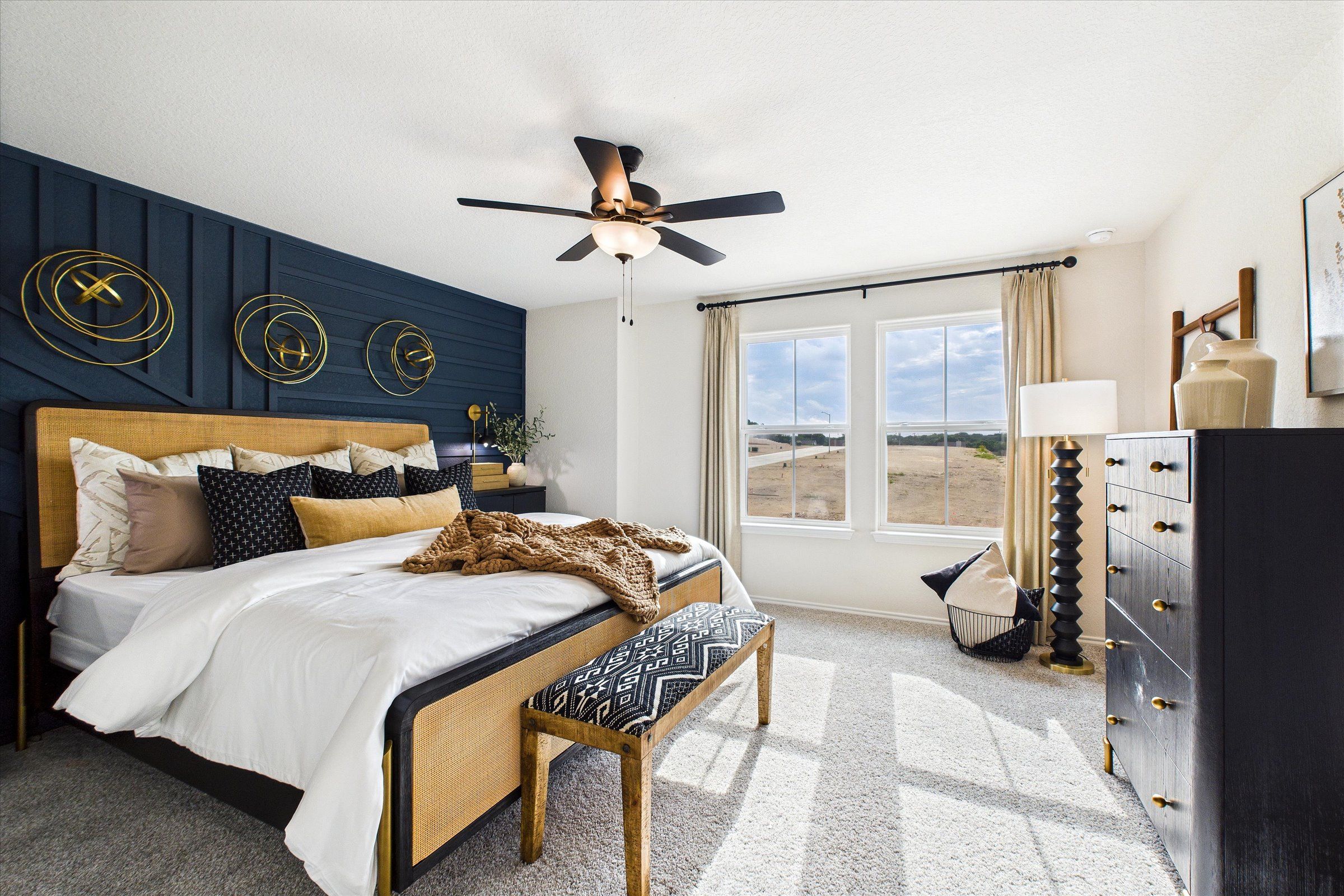 Spacious primary bedroom at Meadows at Oak Creek in San Antonio TX with king bed, navy accent wall, ceiling fan and large windows