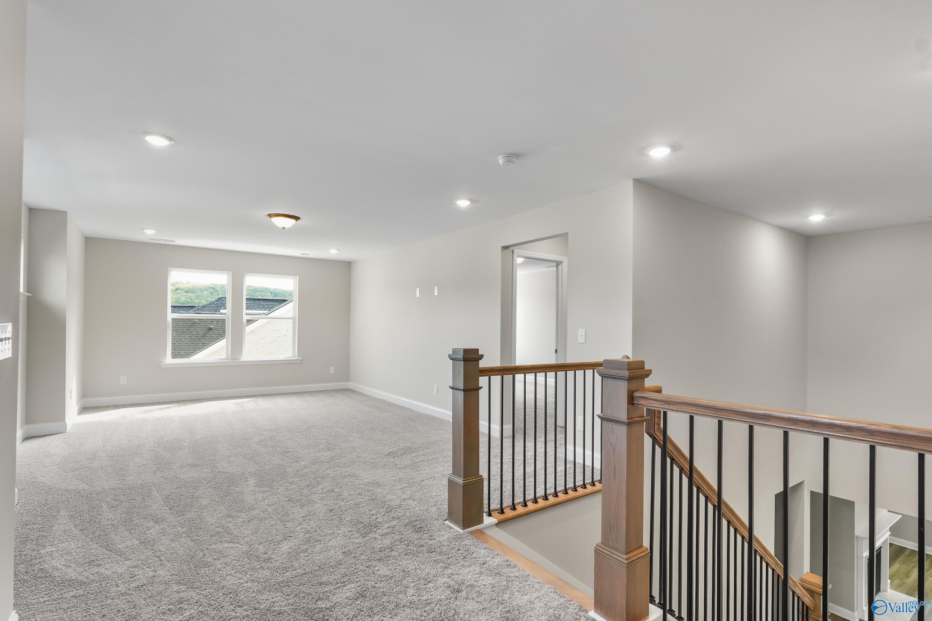 Spacious upstairs loft with gray carpet, large windows, and wooden staircase in Evermore Homes The Haven, Owens Cross Roads, Alabama