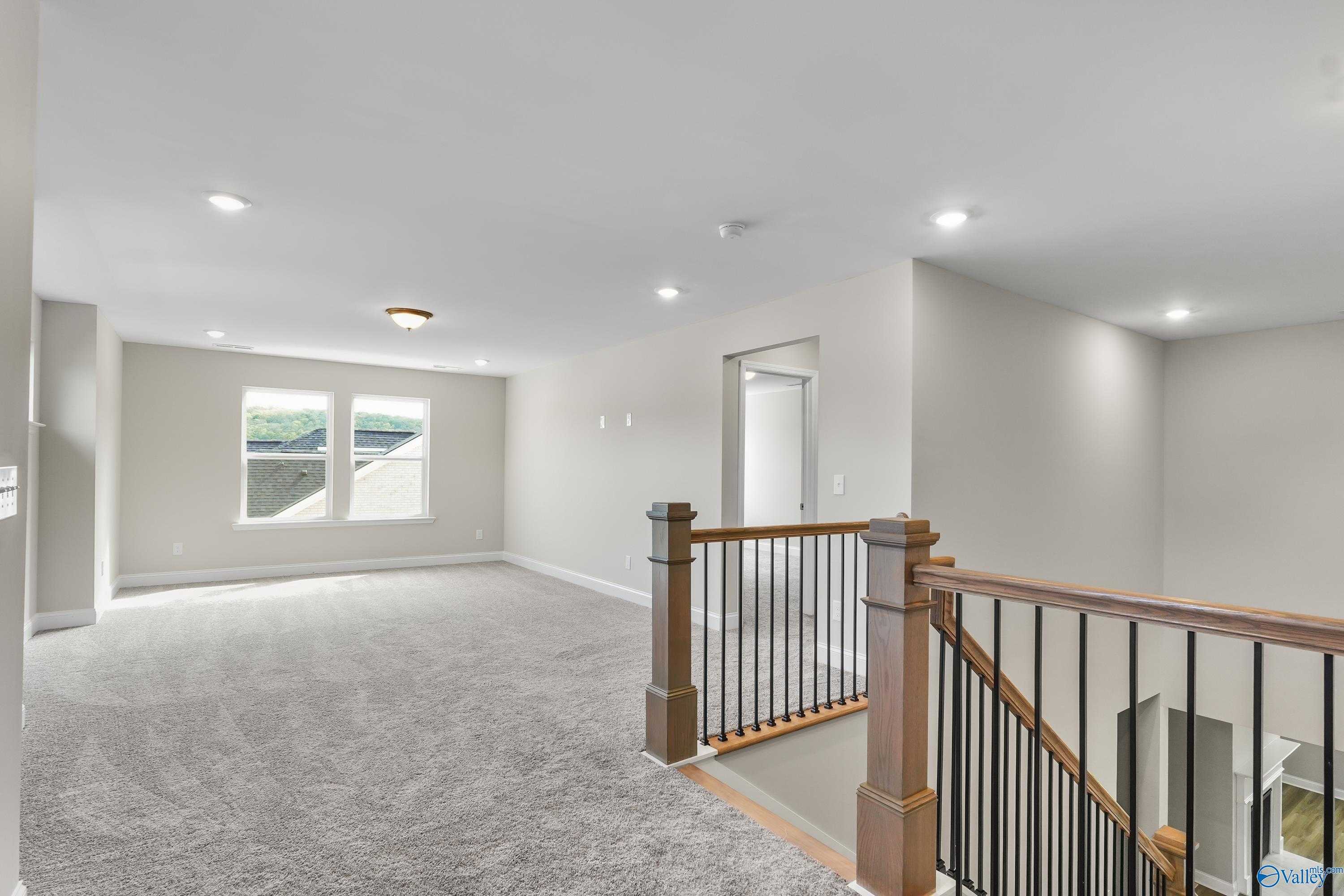 Spacious upstairs loft with gray carpet, large windows, and wooden staircase in Evermore Homes The Haven, Owens Cross Roads, Alabama