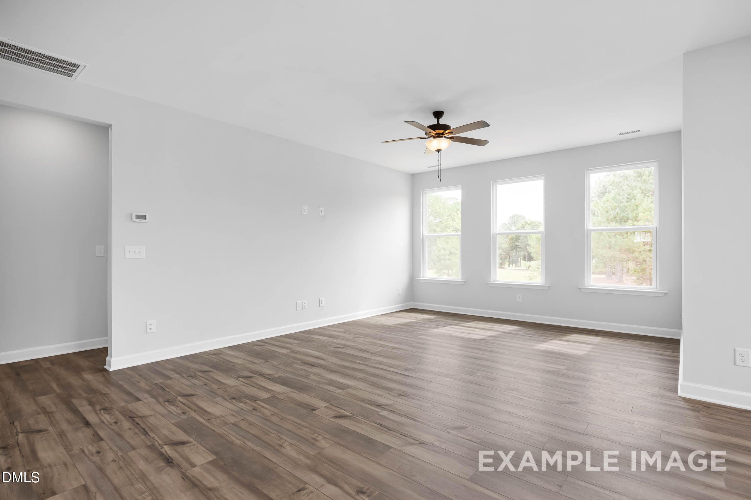 Bright living room with hardwood floors, ceiling fan, and large windows in 3-bedroom Davidson Homes The Ash B, Lillington, NC