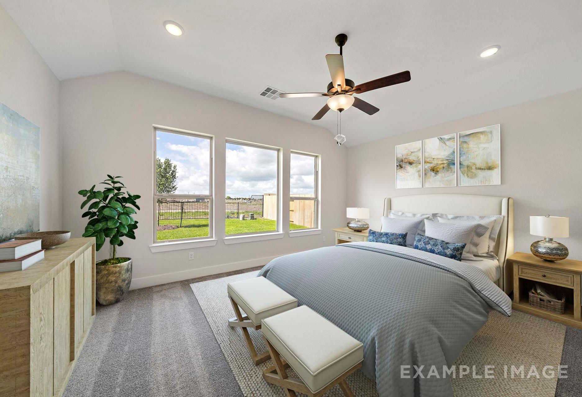 Spacious master bedroom in The Victoria A with king bed, gray bedding, large windows overlooking green pasture, ceiling fan, and modern decor