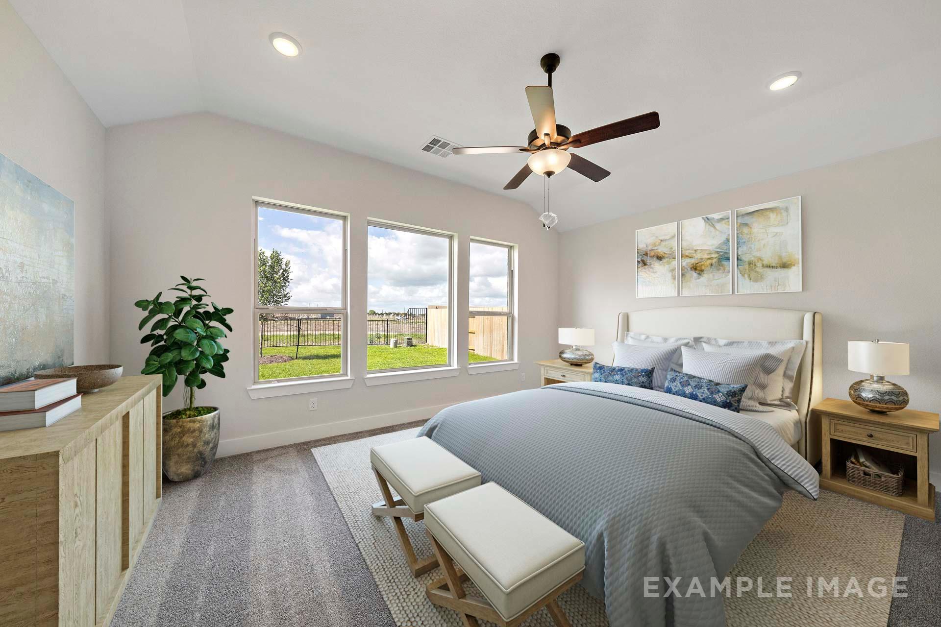 Spacious master bedroom in The Victoria A with king bed, gray bedding, large windows overlooking green pasture, ceiling fan, and modern decor