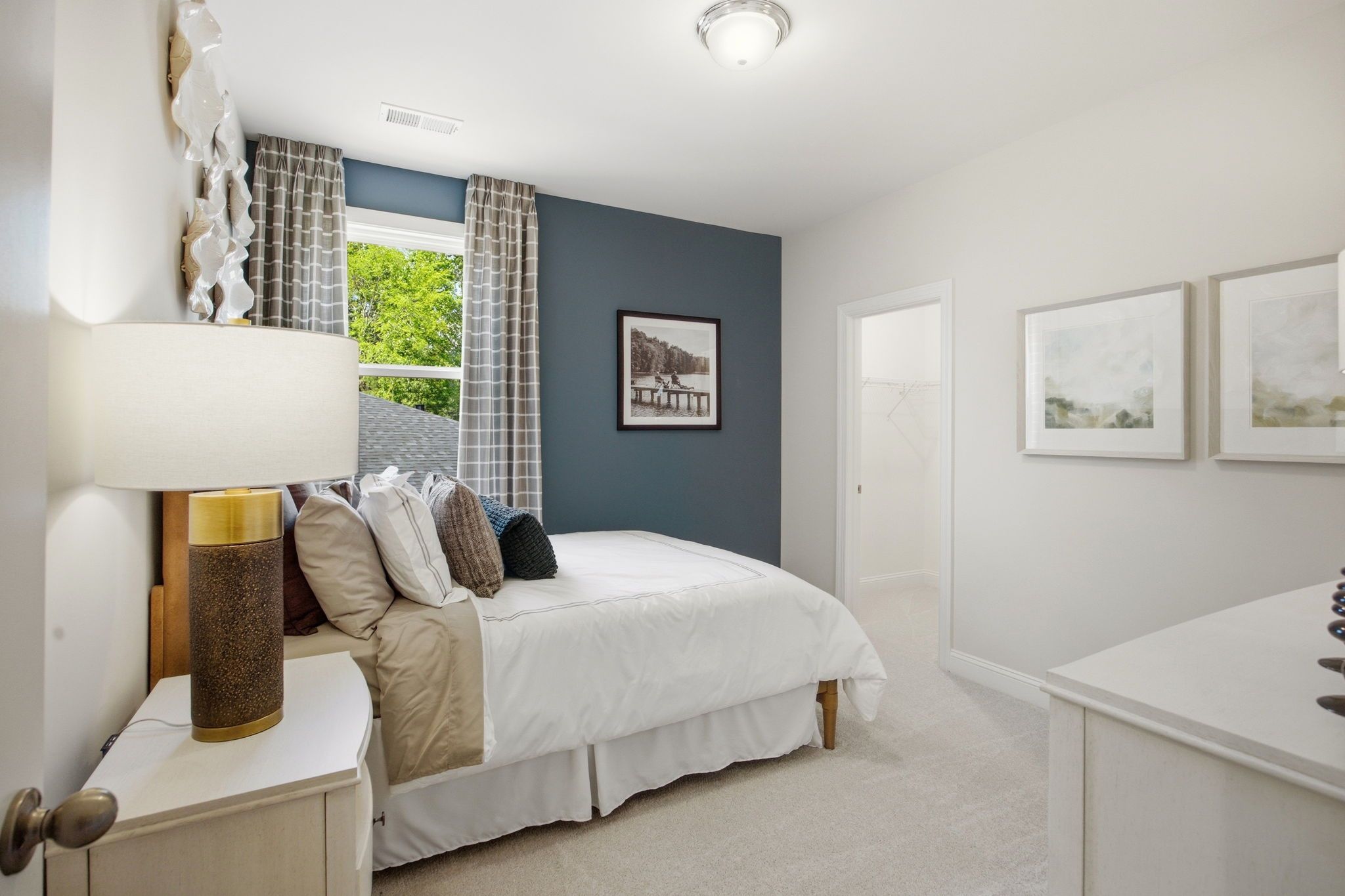 Cozy bedroom at Enclave at Belmont in Belmont NC with navy accent wall, white queen bed, bedside lamp, and window view