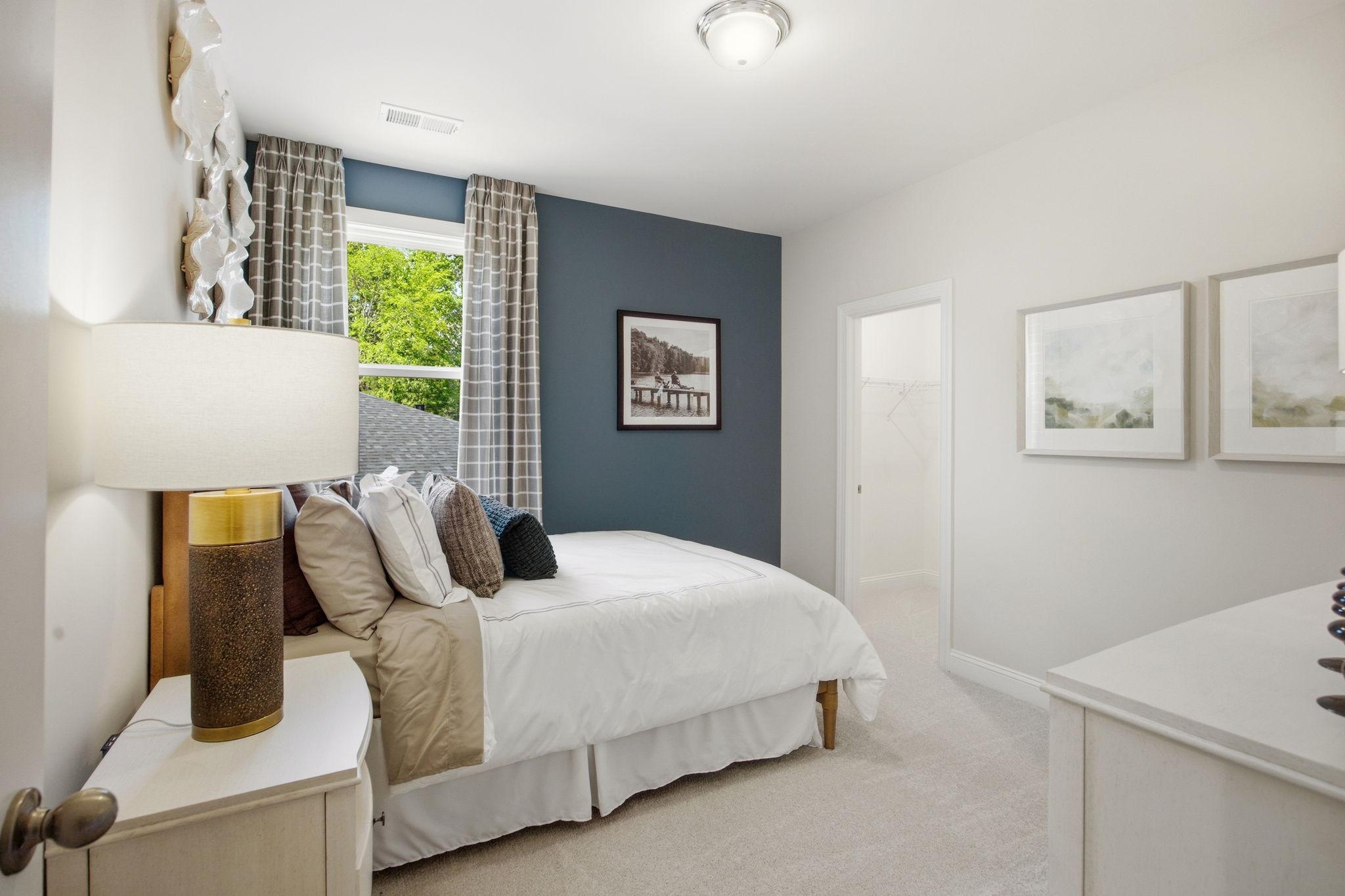 Cozy bedroom at Enclave at Belmont in Belmont NC with navy accent wall, white queen bed, bedside lamp, and window view