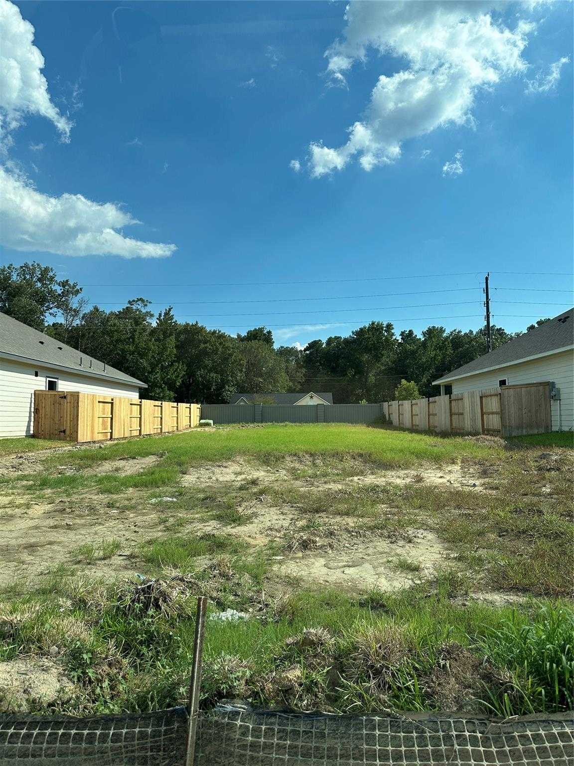 Empty grassy backyard lot with wooden fences, chain-link barrier, and surrounding trees in Sundance Cove, Crosby, Texas for Davidson Homes Everett C