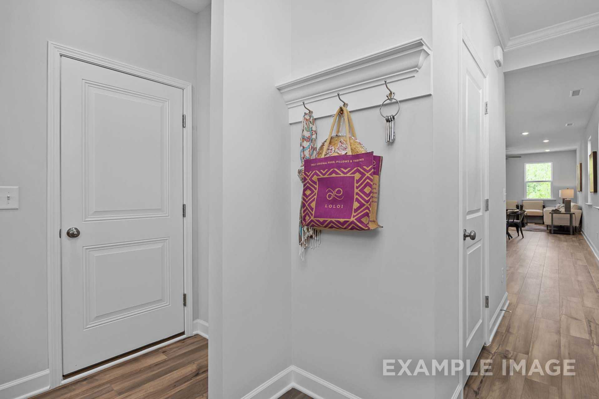 Modern entryway in The Carter B home with white doors, coat hooks holding purple bag and keys, hardwood floors to living area