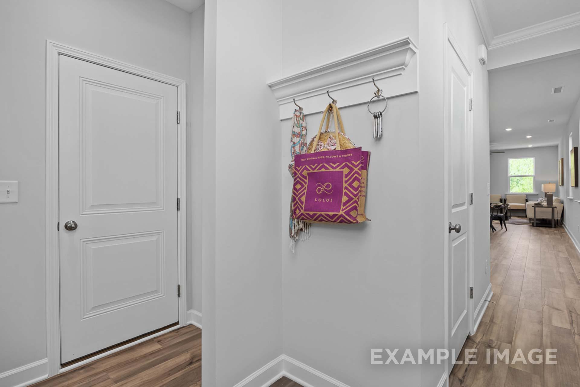 Modern entryway in The Carter B home with white doors, coat hooks holding purple bag and keys, hardwood floors to living area