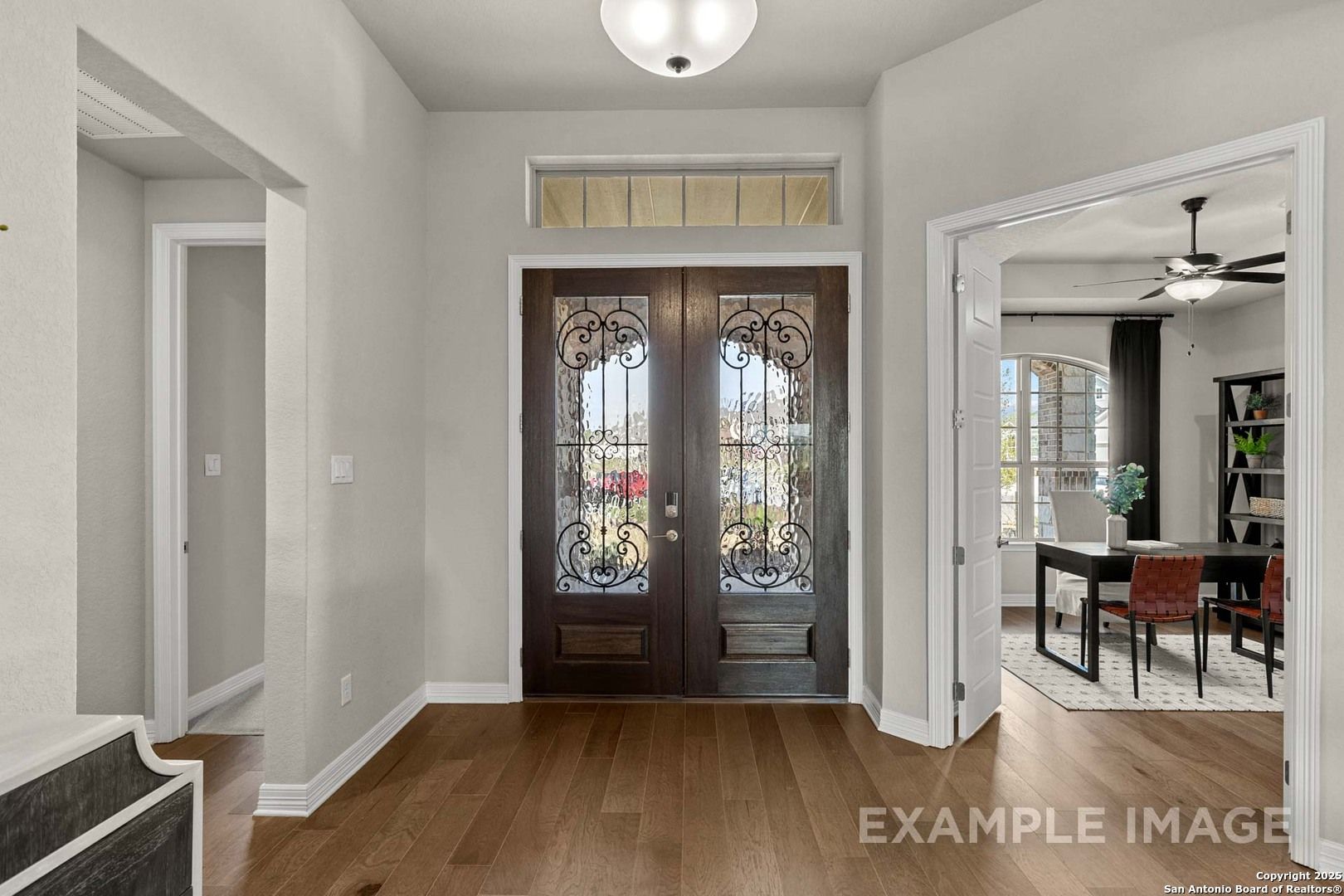 Elegant entry foyer with ornate wood double doors, hardwood floors, and chandelier opening to dining room in Davidson Homes Summerlin B, Castroville, Texas