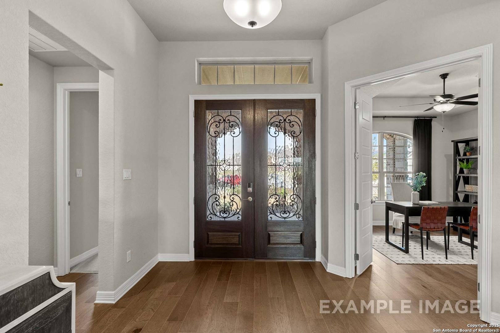 Elegant entry foyer with ornate wood double doors, hardwood floors, and chandelier opening to dining room in Davidson Homes Summerlin B, Castroville, Texas