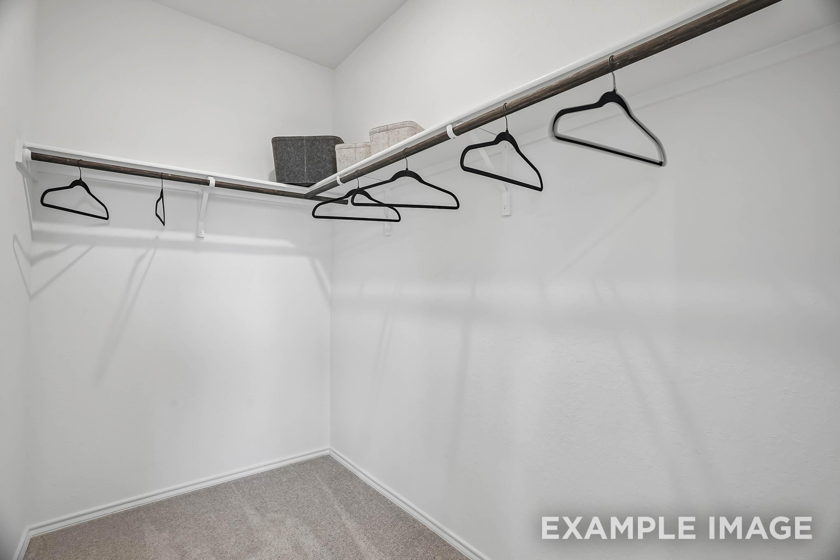 Spacious walk-in closet in The Pinecrest D master suite featuring wall-to-wall shelving and hanging rods.