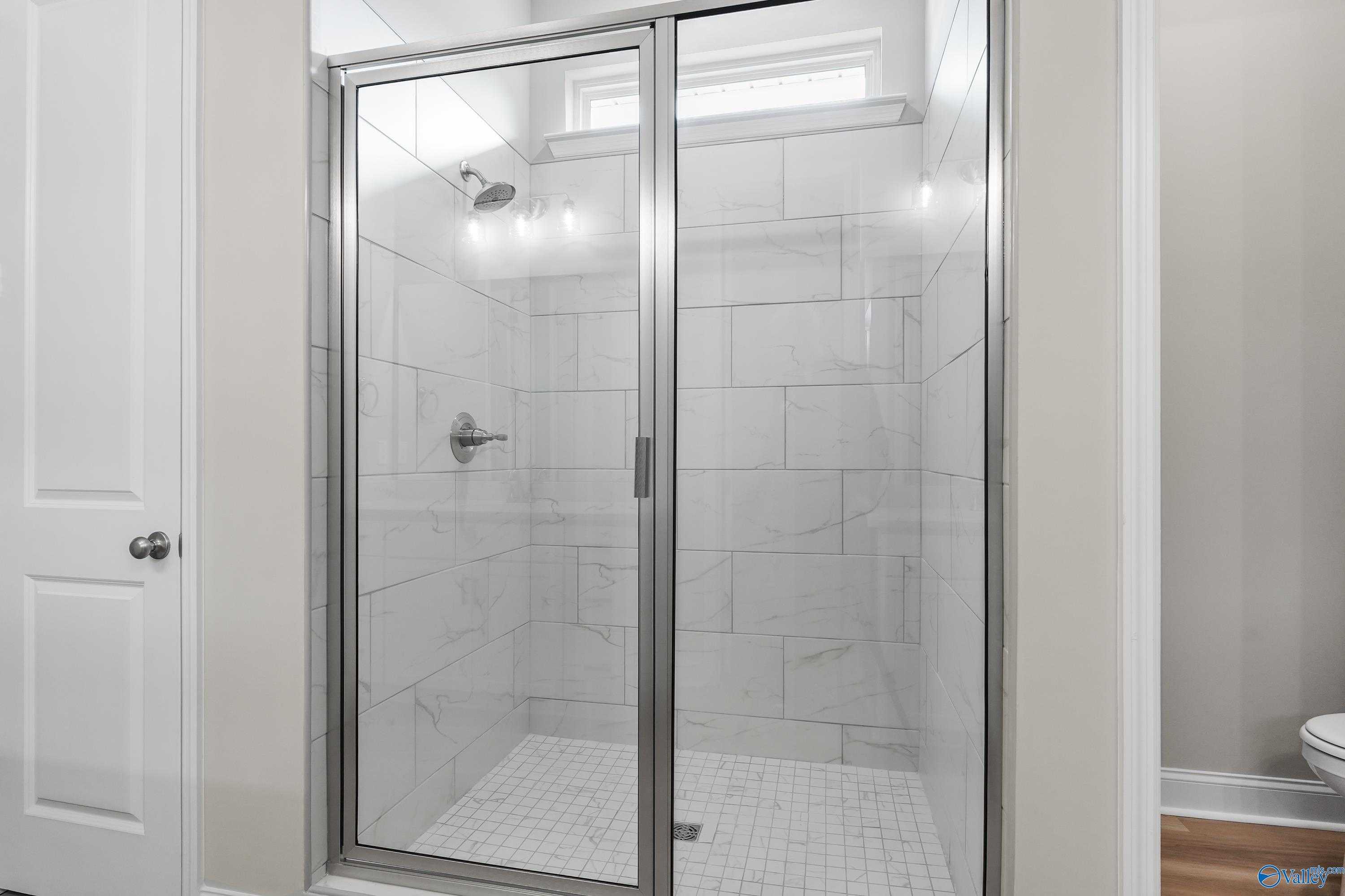 Modern glass shower enclosure with white subway tiles and chrome fixtures in The Haven master bath, Evermore Homes, Owens Cross Roads, AL