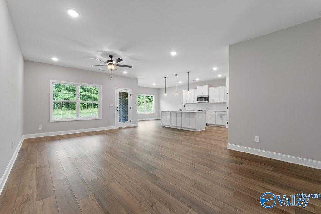Open-concept kitchen-living area with white island, cabinets, hardwood floors, and large windows in Davidson Homes Montgomery B, Hartselle AL