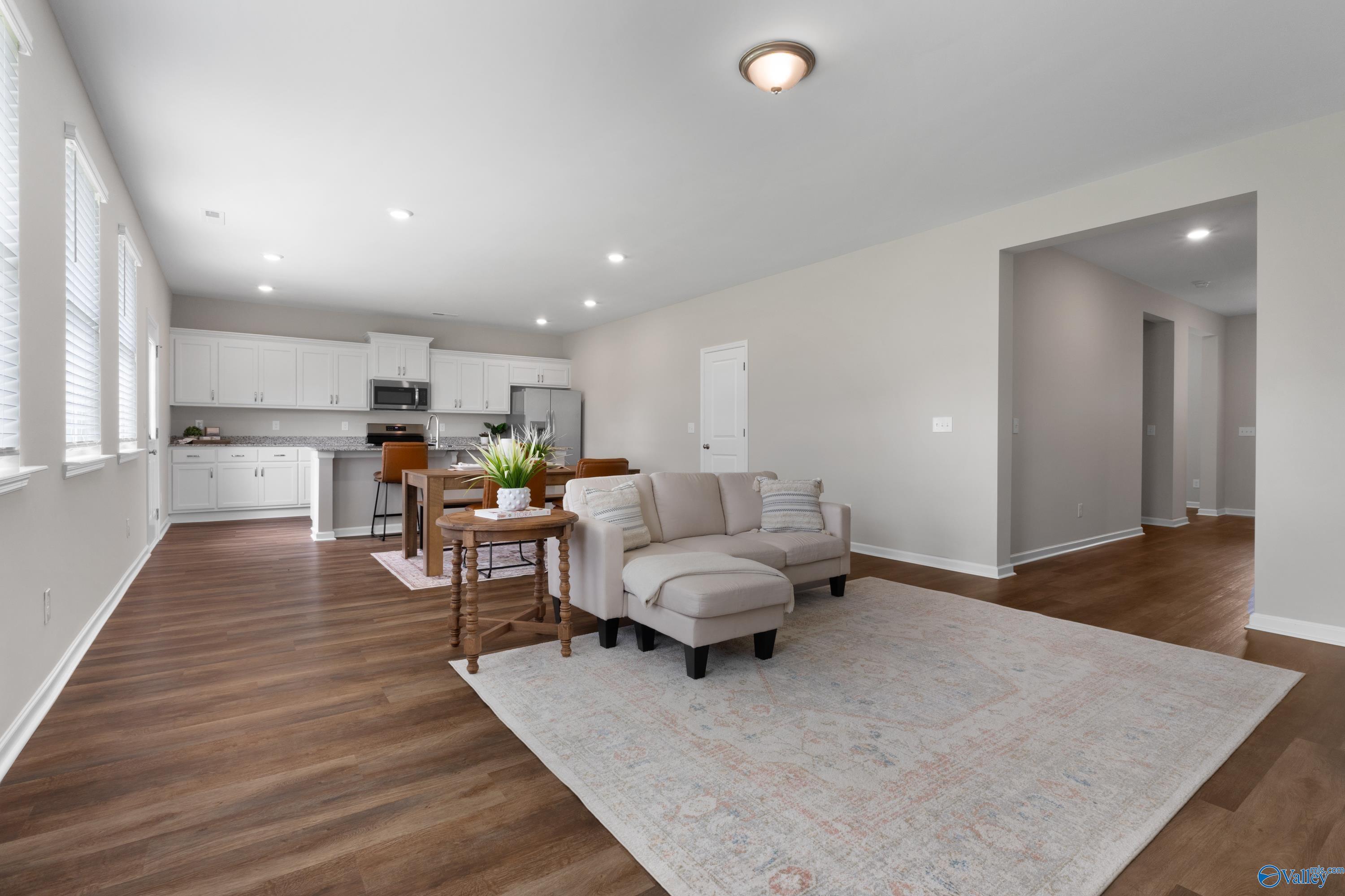 Open-concept living room with white kitchen cabinets, beige sofa, hardwood floors, and area rug in The Noble floor plan, Madison, Alabama