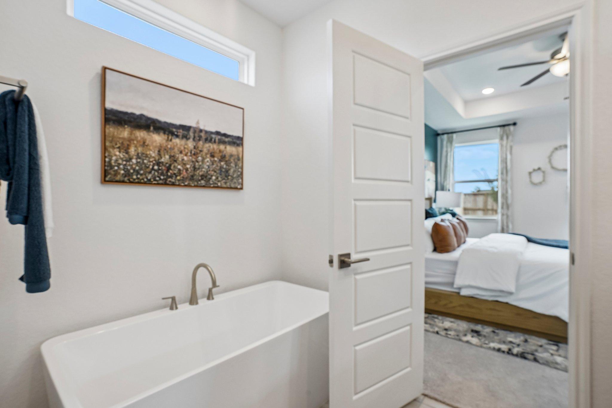 Modern soaking tub in a primary bathroom at Morgan Meadows in San Antonio, Texas, with a view into the bedroom.