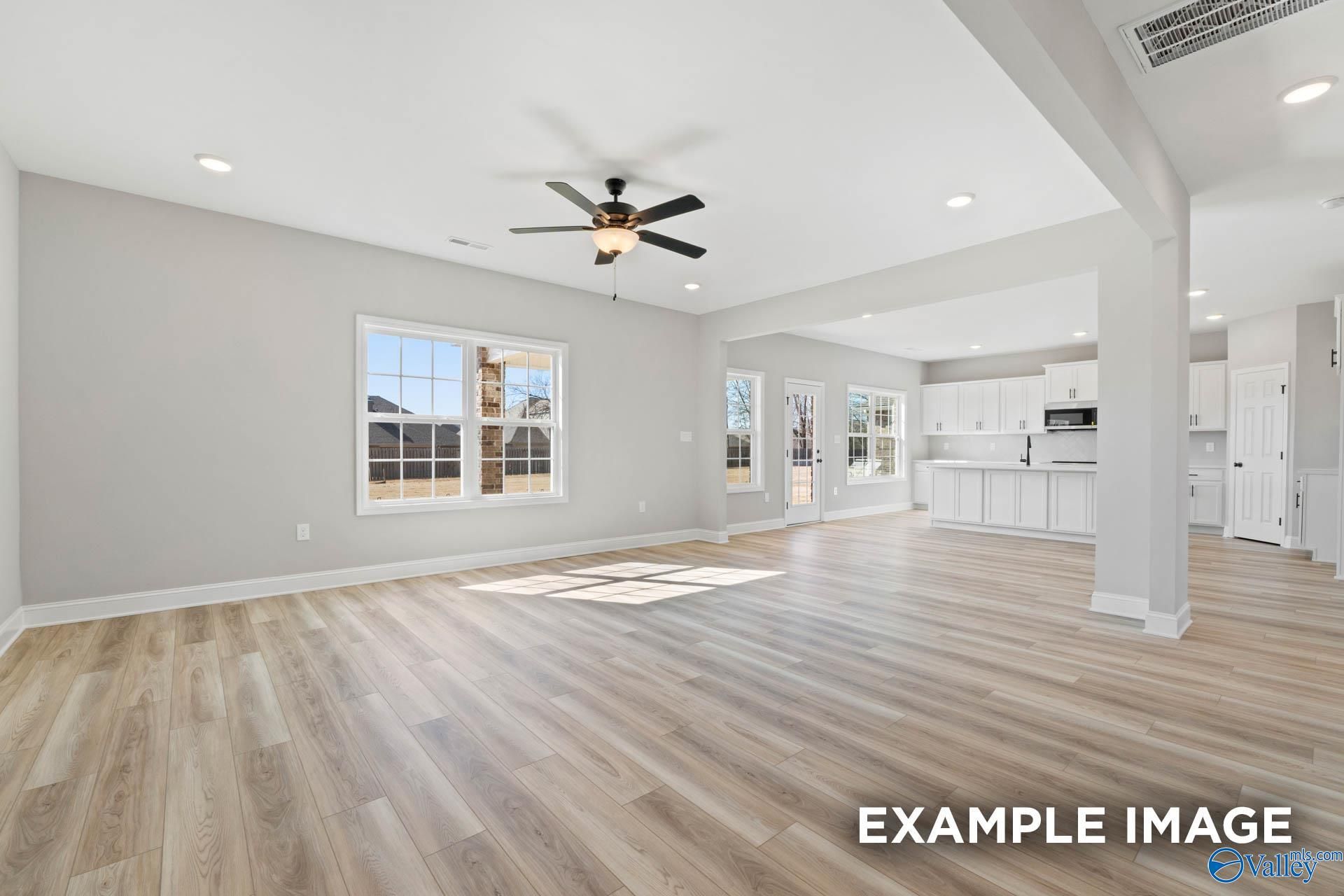 Open-concept living room with light luxury vinyl plank floors, ceiling fan, and view of kitchen in Madison, Alabama home.