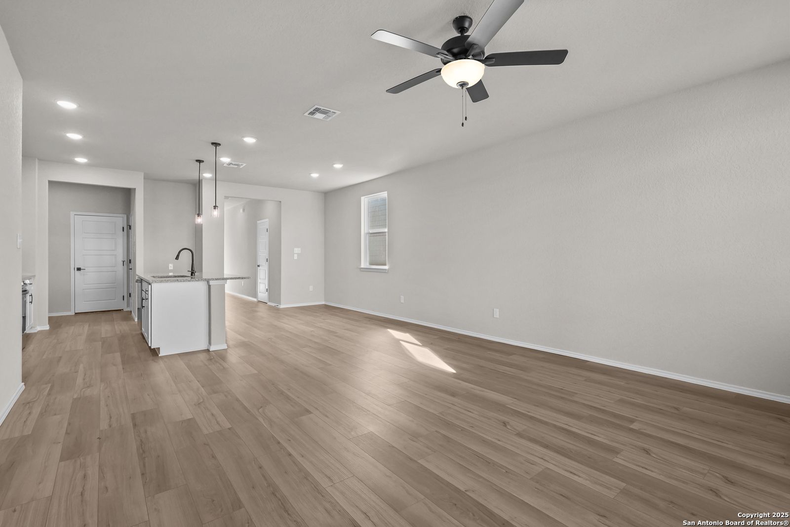 Modern open kitchen with white island sink, hardwood floors, and ceiling fans in Davidson Homes The Brazos C, San Antonio