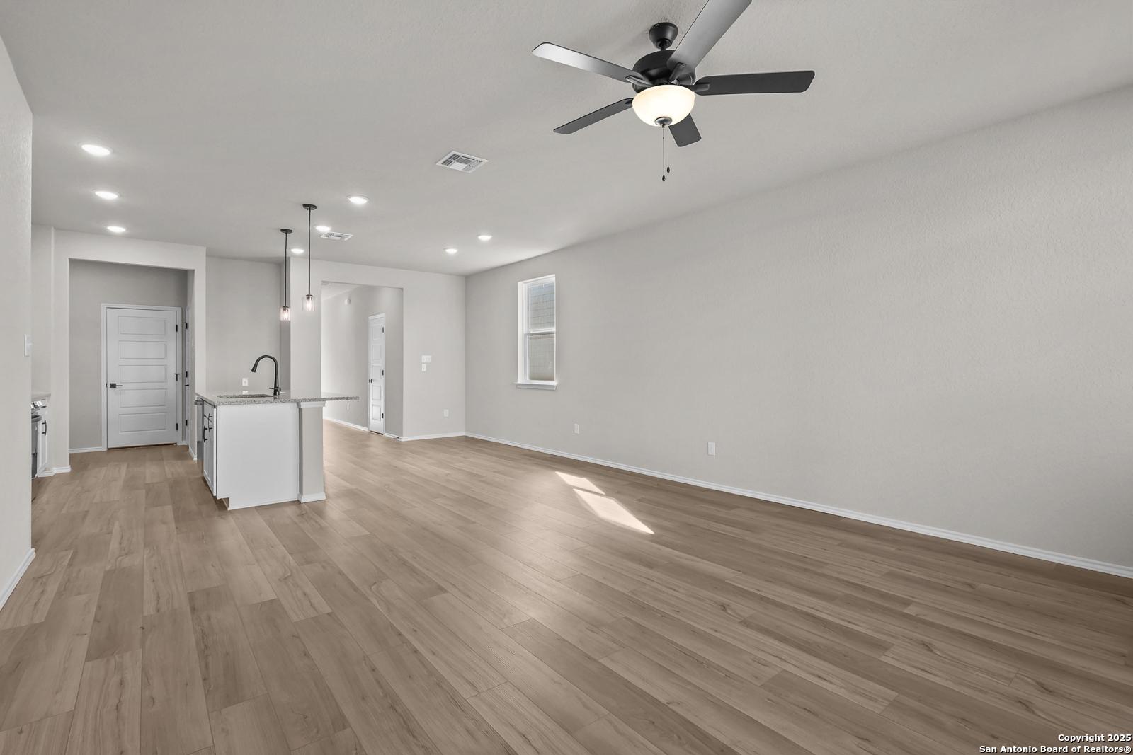 Modern open kitchen with white island sink, hardwood floors, and ceiling fans in Davidson Homes The Brazos C, San Antonio