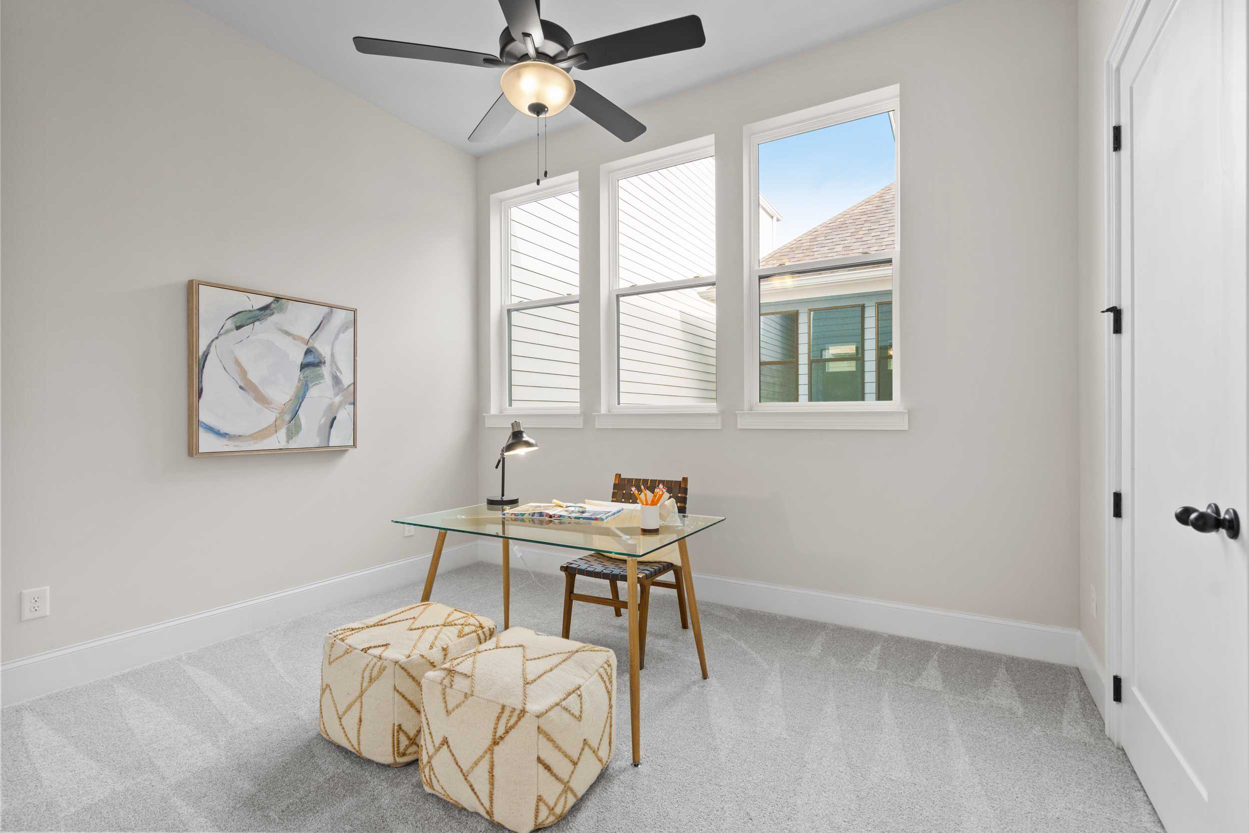 Cozy home office at The Village at Towne Lake in Woodstock GA with glass desk, ceiling fan, abstract art, and large windows