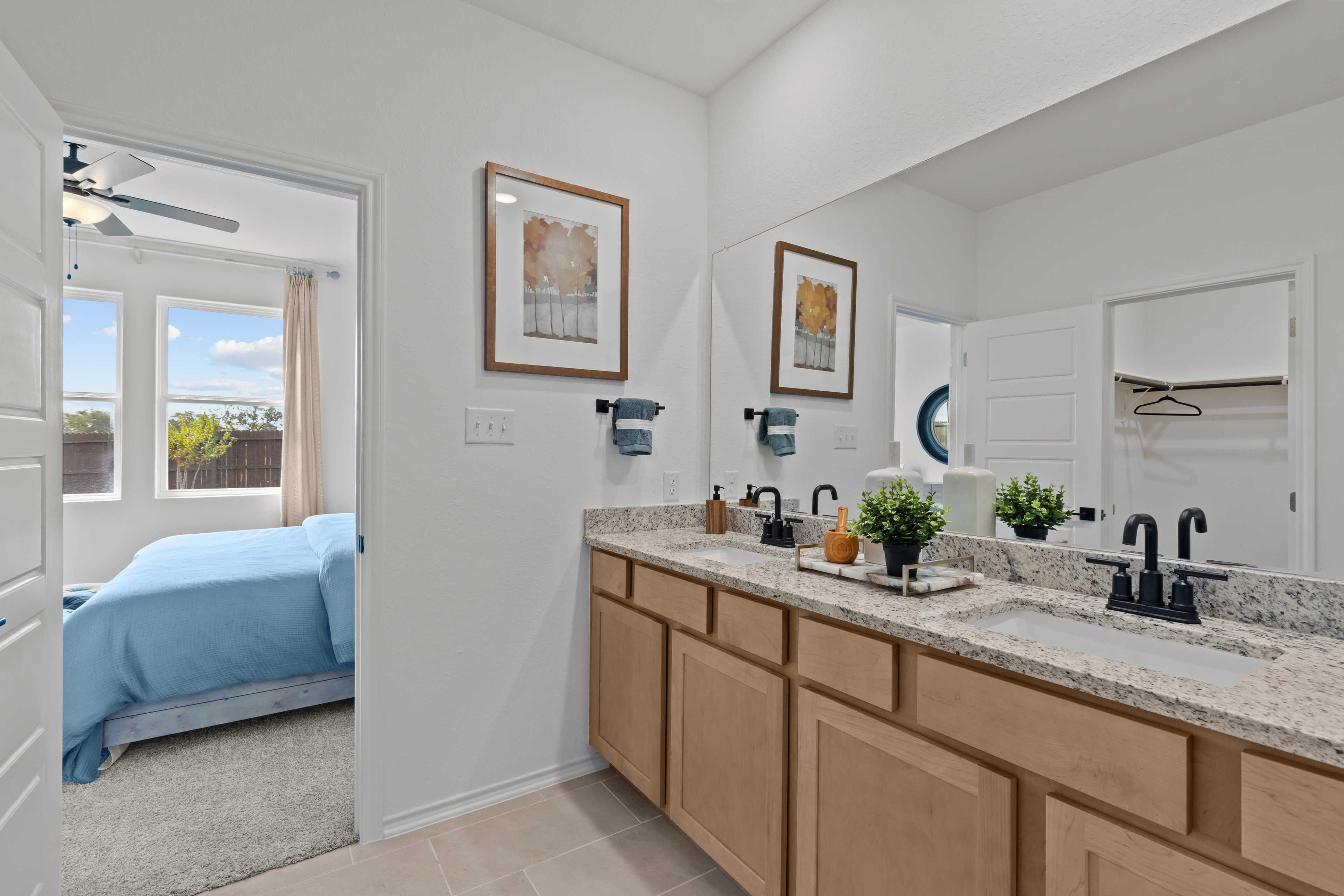Spacious master bathroom in The Douglas C with double vanity, granite counters, framed art, and bedroom view