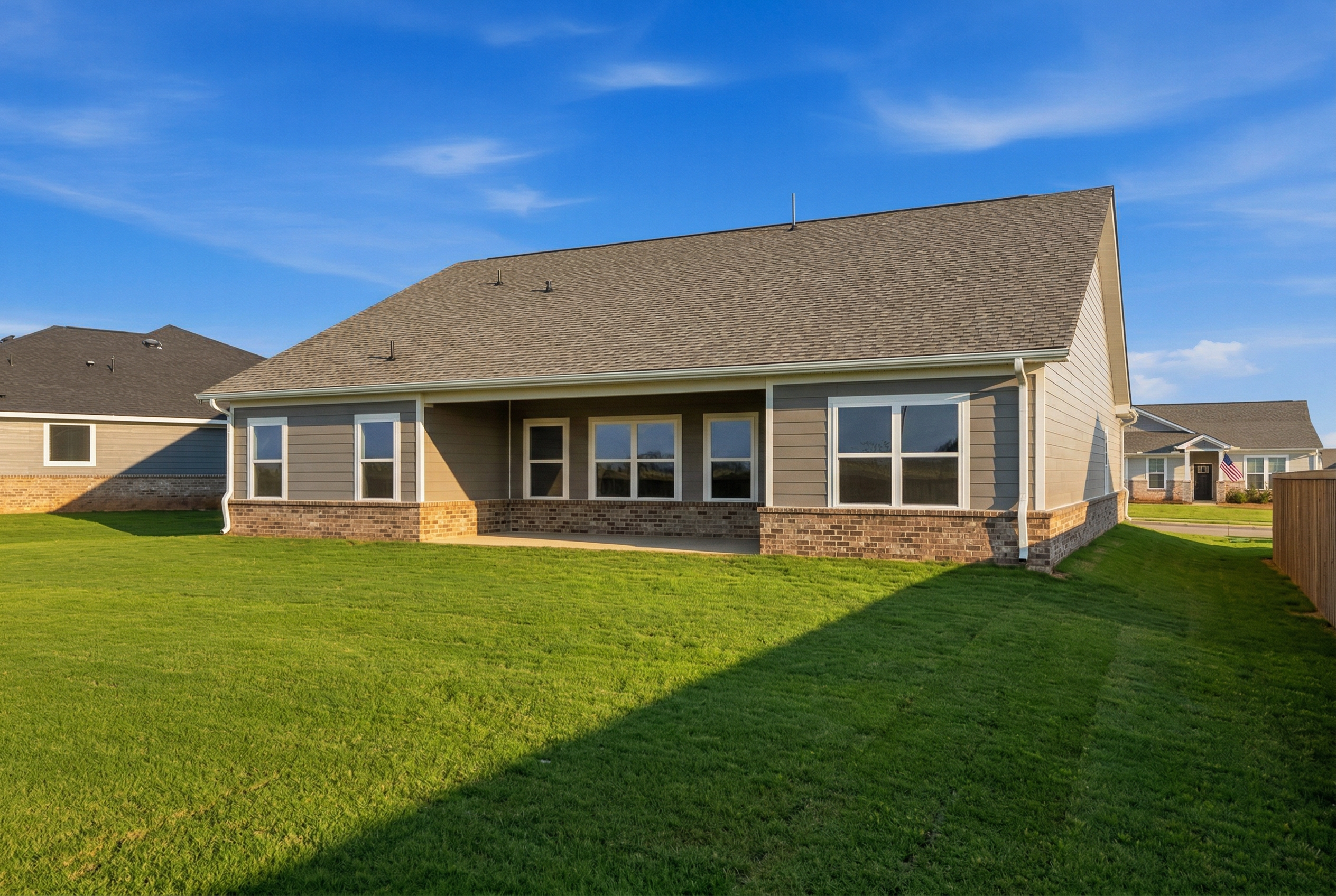 Rear elevation of The Rockford single-story home with stone siding, large windows, covered patio, and lush green yard in Cullman, AL