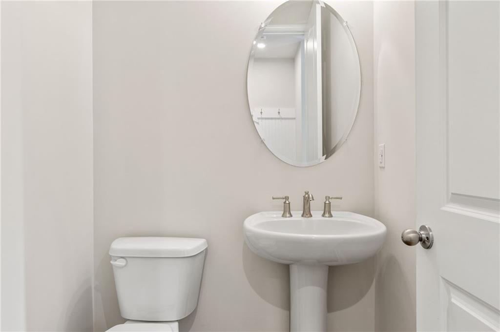 Modern powder room with white pedestal sink, chrome faucet, oval mirror, and toilet in Davidson Homes The Danbury E, Buford, GA