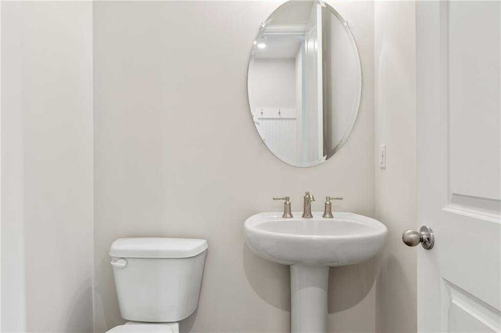 Modern powder room with white pedestal sink, chrome faucet, oval mirror, and toilet in Davidson Homes The Danbury E, Buford, GA