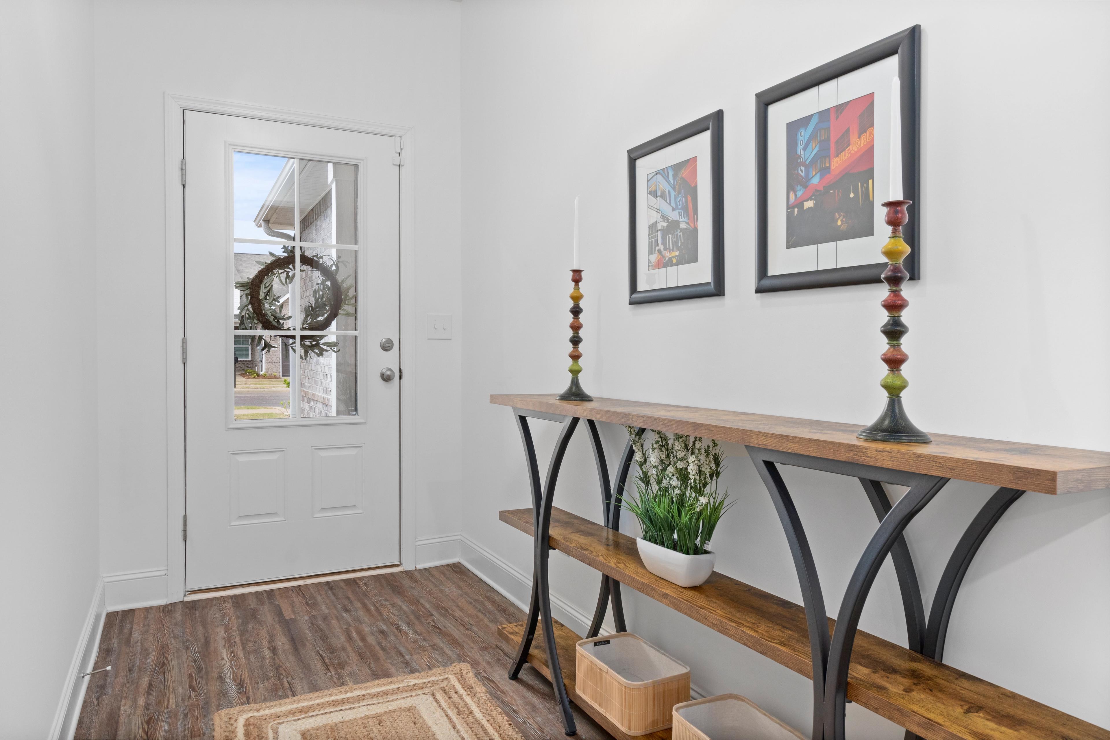 Welcoming entryway in The Cumberland Davidson Homes design with glass-paneled door, holiday wreath, wooden console table, potted plant, and abstract art