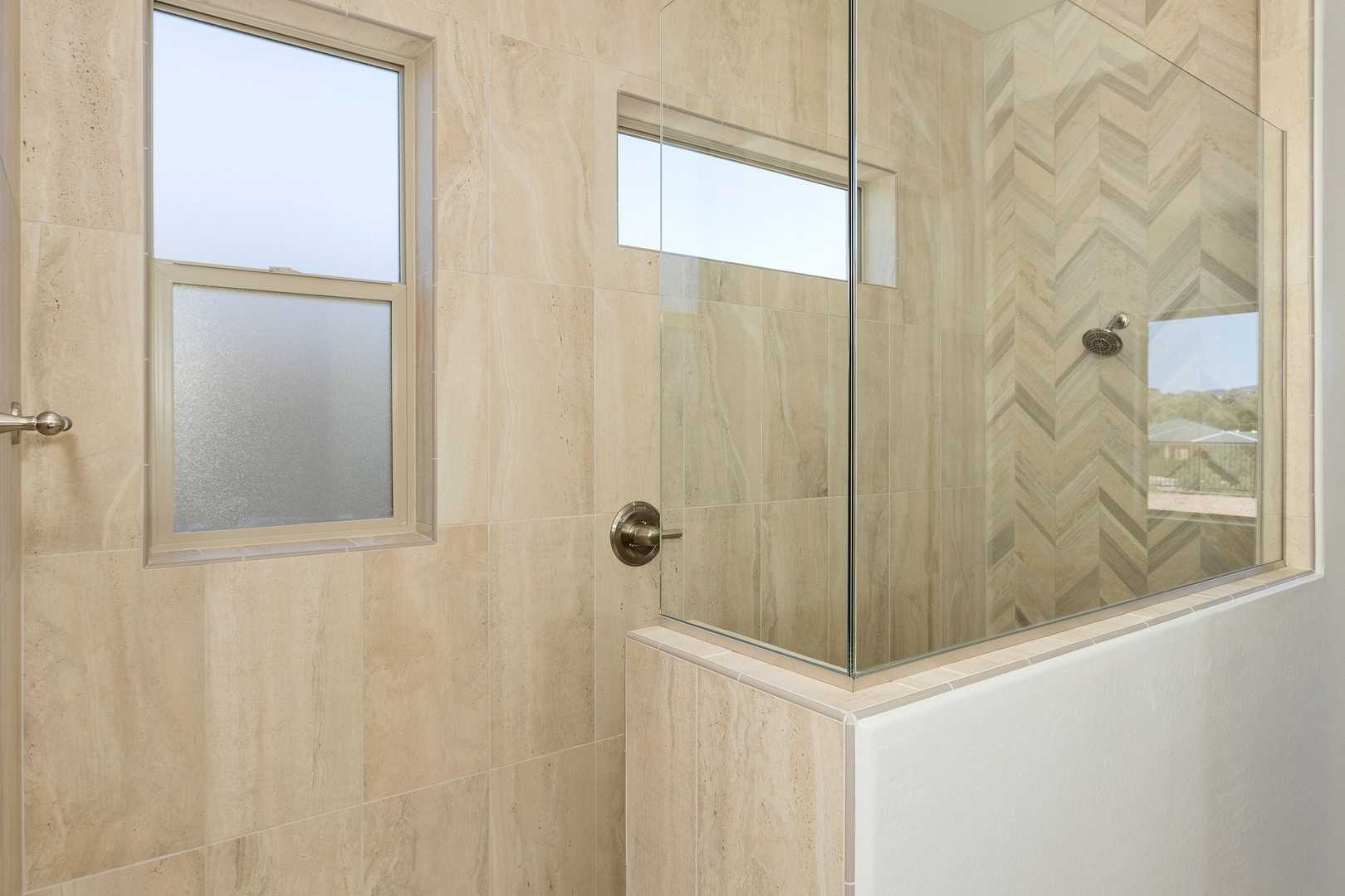 Modern master bathroom shower in The Daybreak by Davidson Homes, featuring frameless glass enclosure, herringbone tile accents, and frosted windows