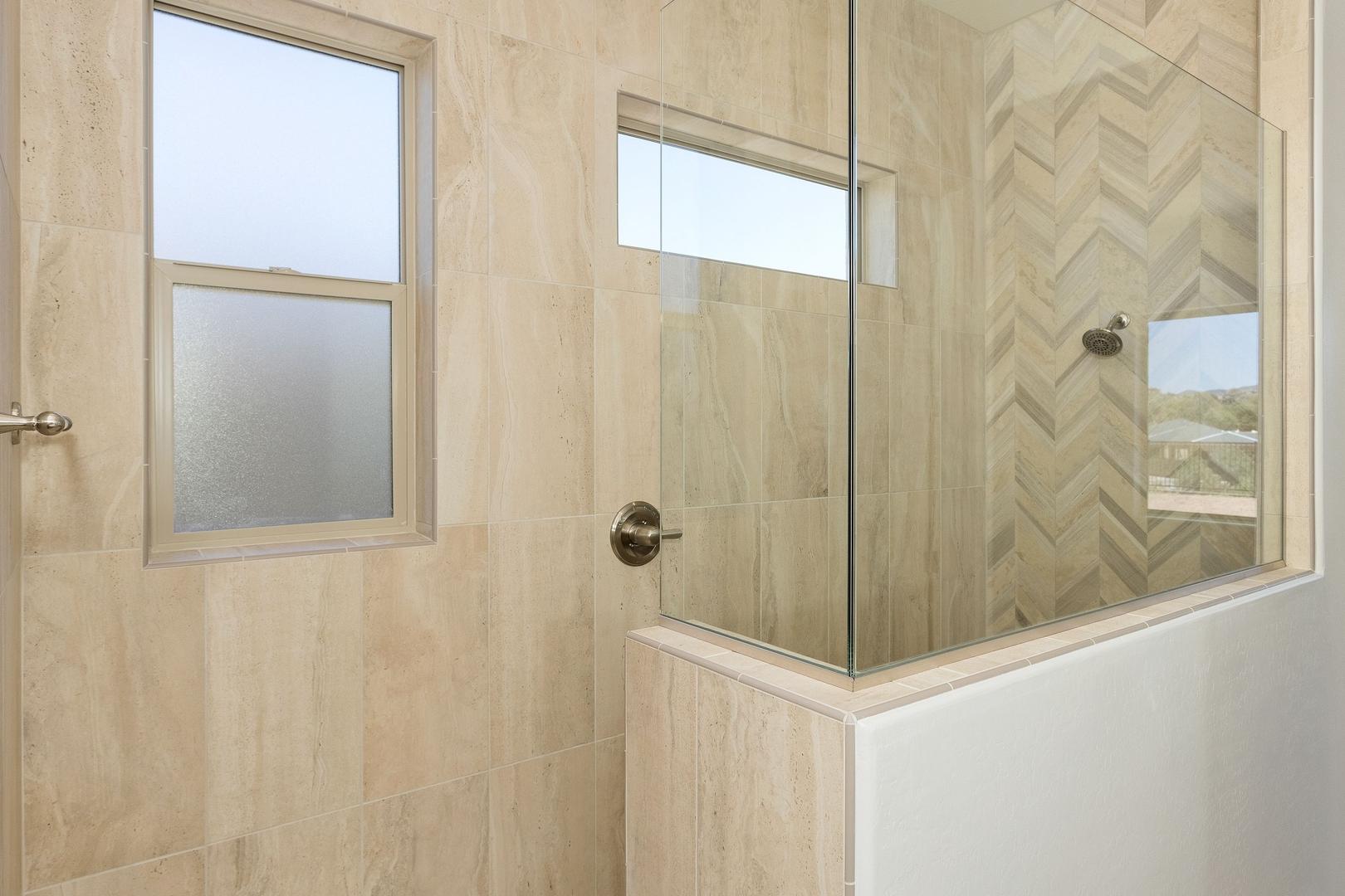Spacious master shower in The Daybreak E home with herringbone tile walls, frameless glass enclosure, and frosted windows