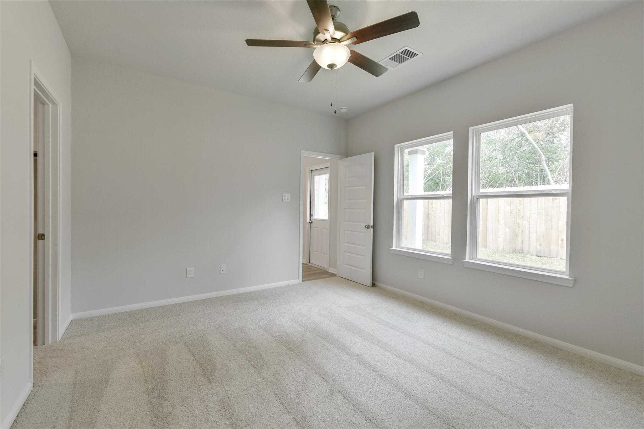 Bright secondary bedroom with ceiling fan, large windows overlooking backyard, and carpeted floors in Davidson Homes The Frio G, Conroe, Texas