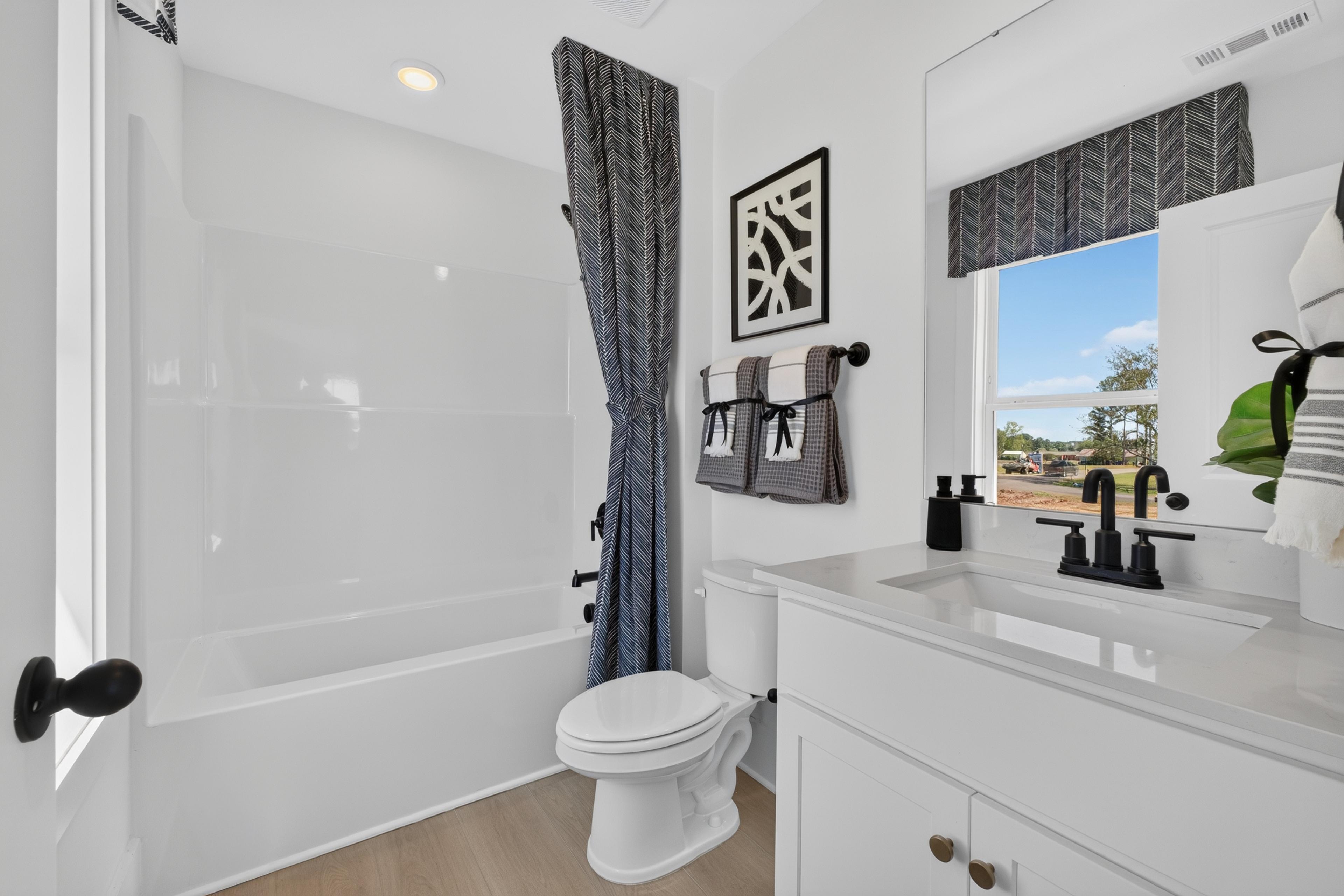 Bright white bathroom with soaking tub, black matte fixtures, and marble vanity at Evergreen Mill in Madison, Alabama by Davidson Homes.