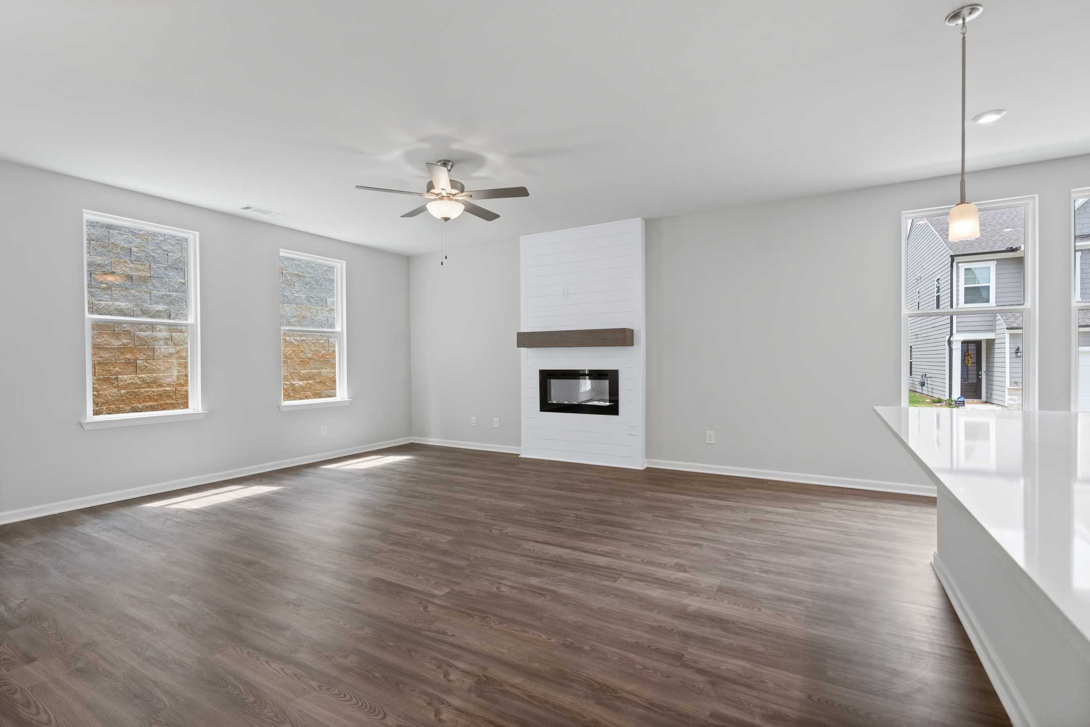 Open-concept great room in The Cary A with white fireplace, hardwood floors, large windows, and ceiling fan