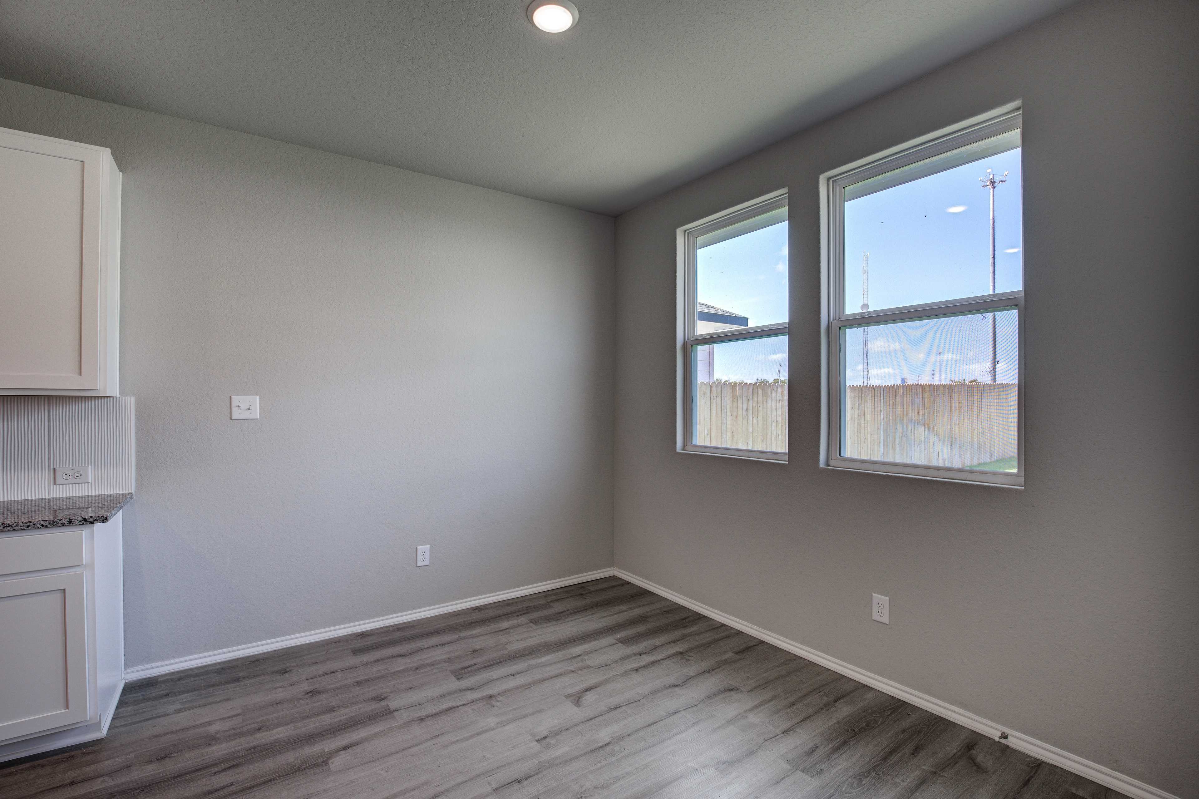 Bright laundry room in The Asheville home design featuring gray walls, white cabinets, quartz sink countertop, and large dual windows with backyard view