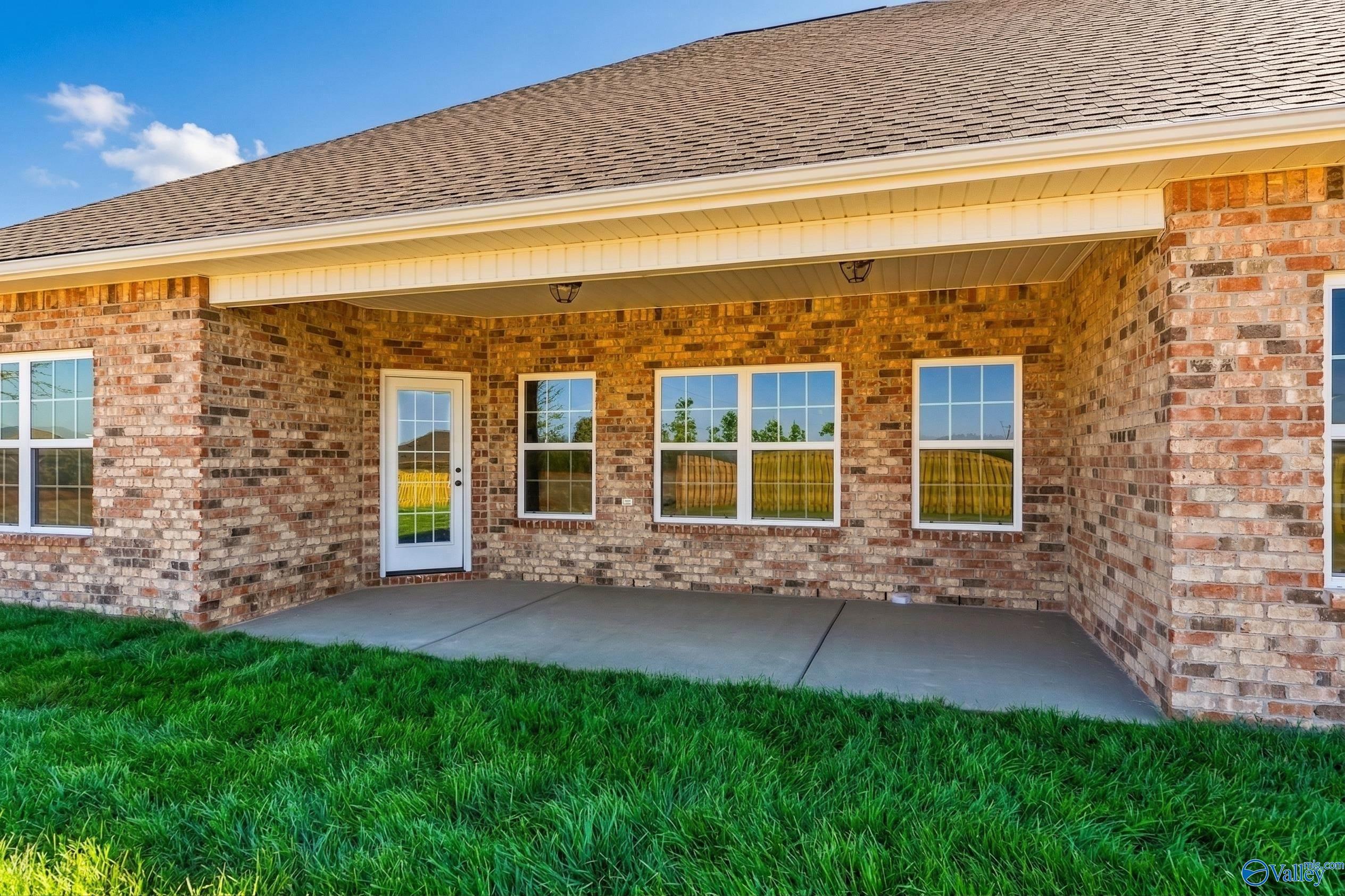 Covered back patio with brick exterior, large windows, and lush green lawn in Davidson Homes The Rockford, Creekside, Harvest, Alabama