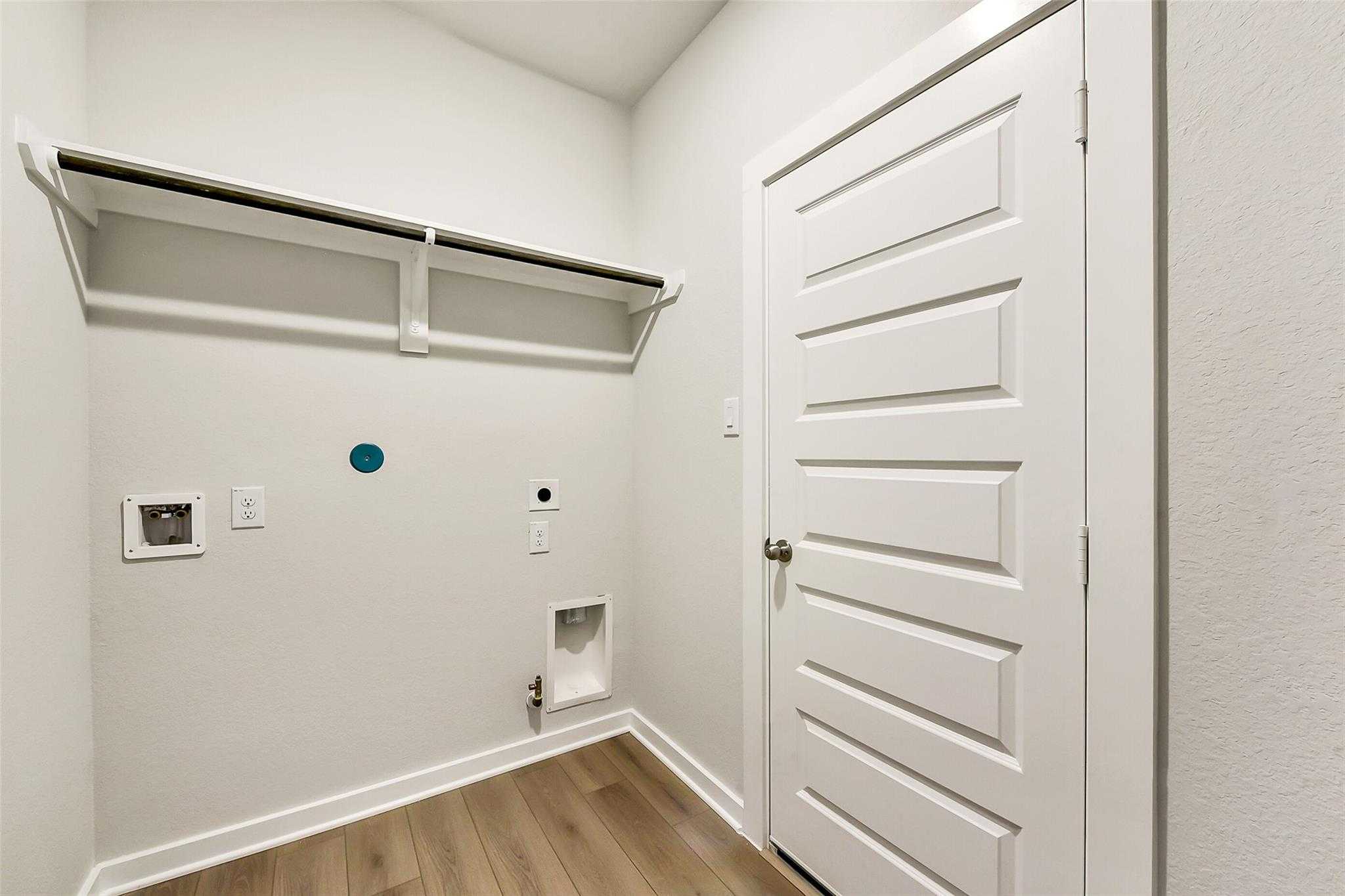 Spacious laundry room with built-in shelves, washer-dryer hookups and wooden floors in Davidson Homes The Frio G, Dayton Texas