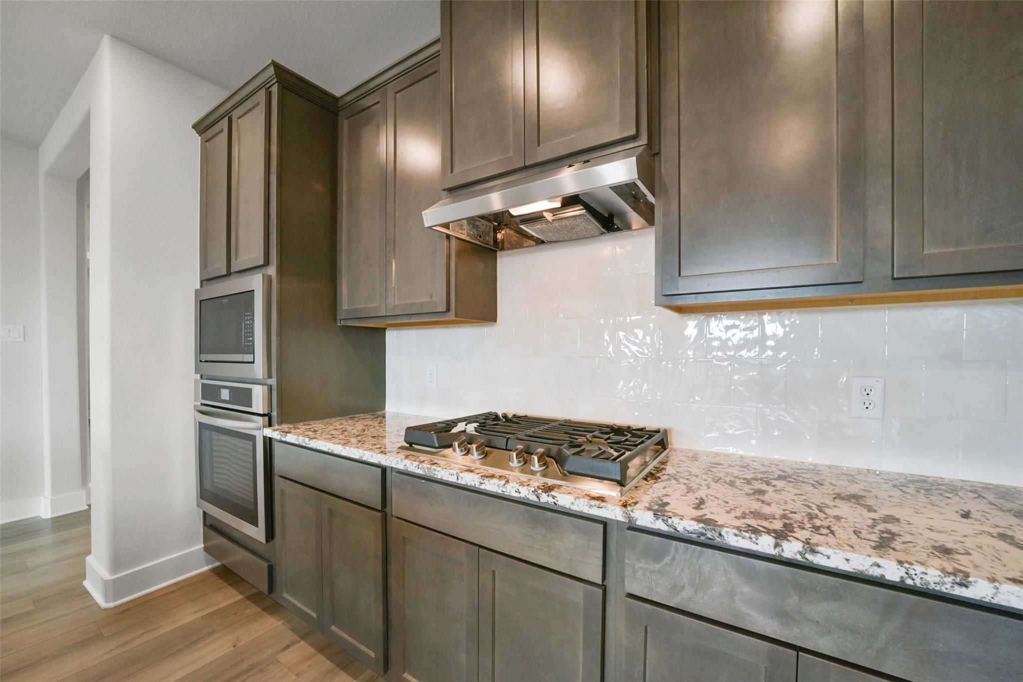 Modern kitchen with gray shaker cabinets, speckled quartz counters, stainless double oven, gas cooktop in Davidson Homes Zion A, Texas City