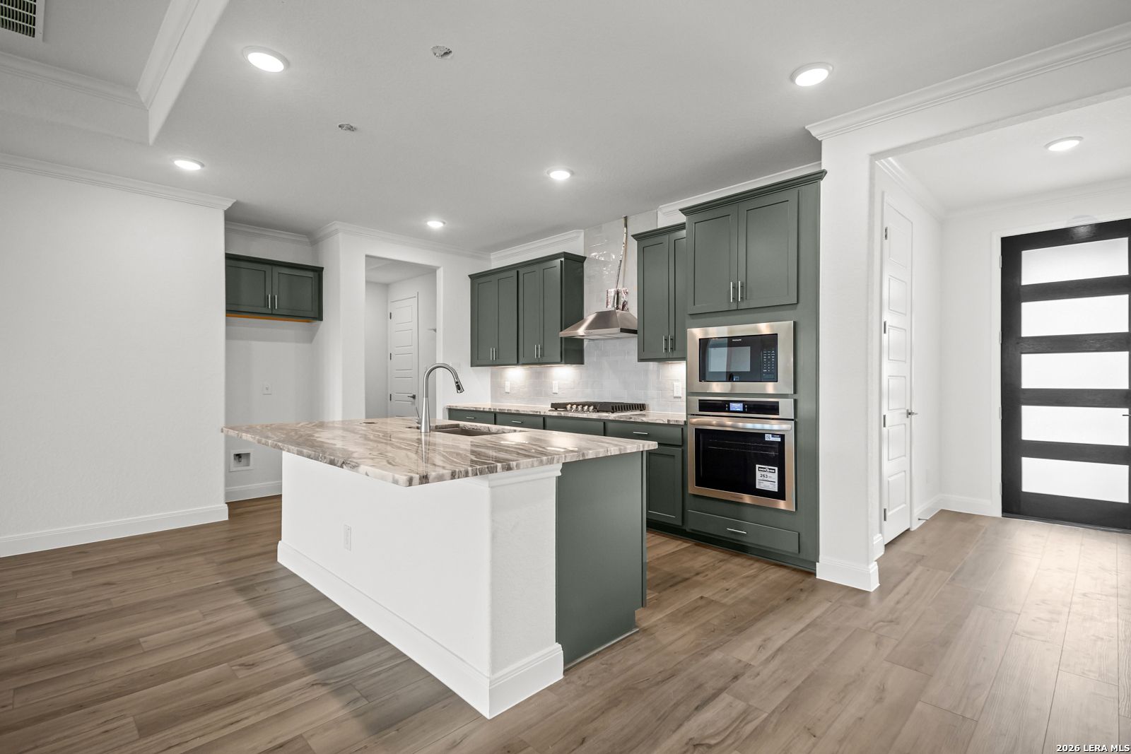 Modern kitchen with dark green cabinets, marble island, and stainless appliances in The Lanier G home, Castroville, TX.