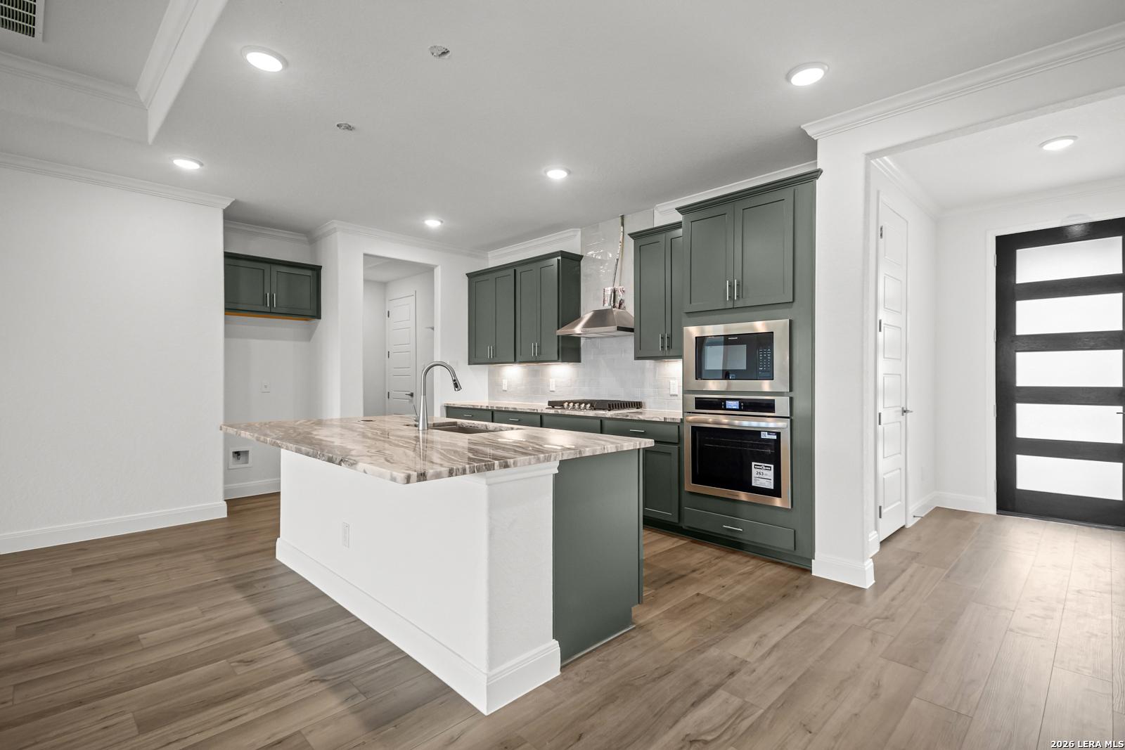 Modern kitchen with dark green cabinets, marble island, and stainless appliances in The Lanier G home, Castroville, TX.